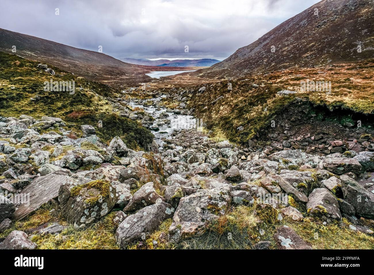 Ein Bach, der durch ein felsiges Tal fließt. Der Fluss ist von Felsen umgeben, die mit Moos und Gras bedeckt sind. Das Tal ist schmal und steil, mit Hügeln risi Stockfoto