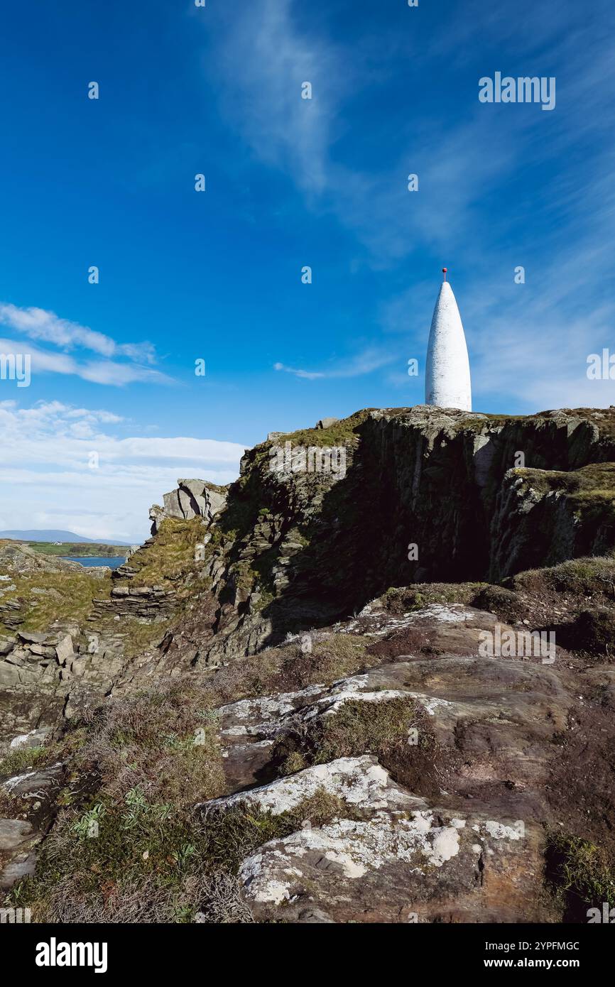 Eine hohe, weiße, konische Struktur steht auf einer felsigen Klippe vor einem klaren blauen Himmel. Dünne Vegetation bedeckt die Klippe. Stockfoto