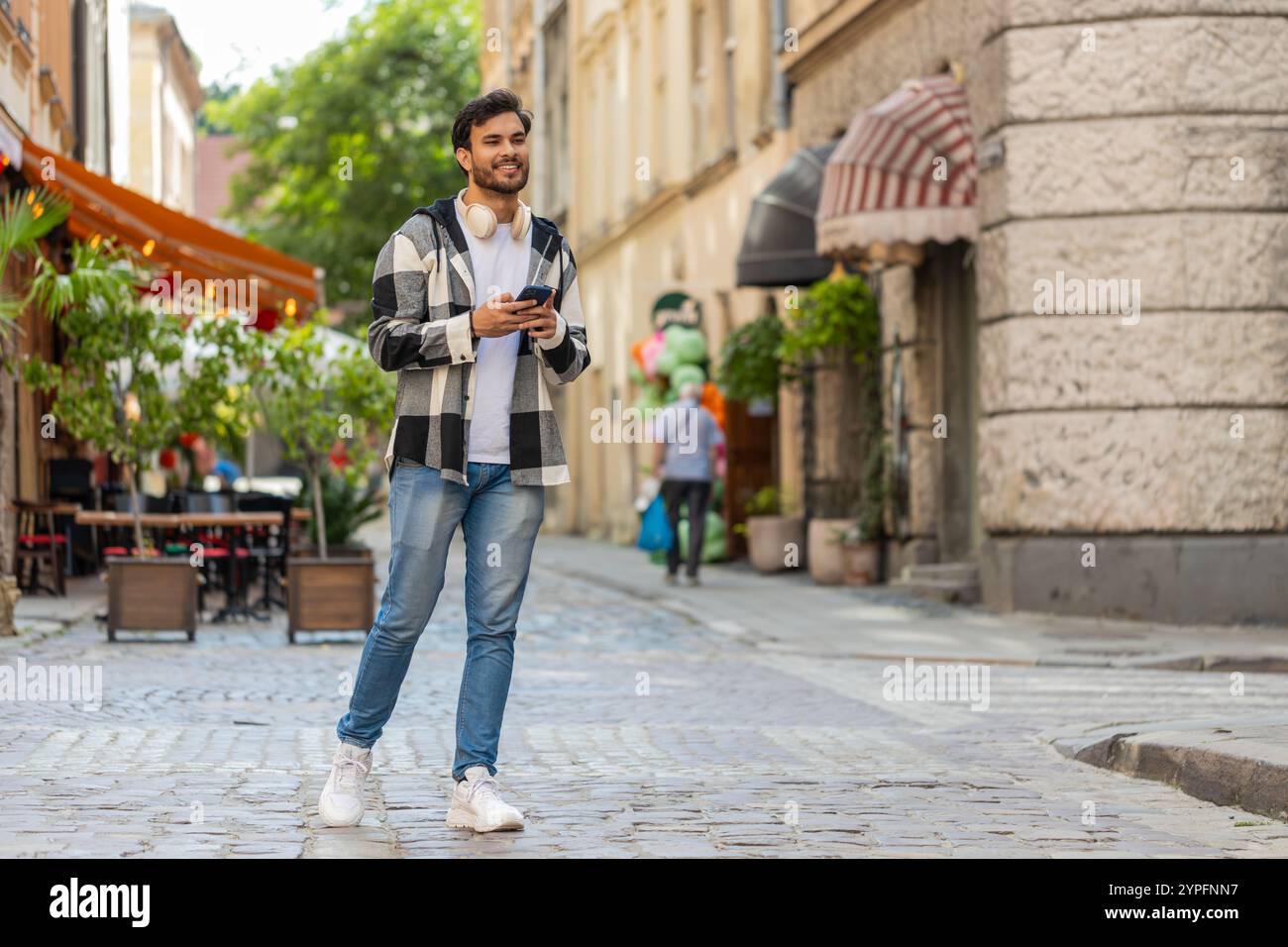 Junger Mann, der ein Smartphone benutzt, um Textnachrichten einzugeben und im Freien in der mobilen Navigations-App nach einem Weg auf der Karte zu suchen. Hispanischer Mann, der an der Stadtstraße vorbeigeht. Stockfoto