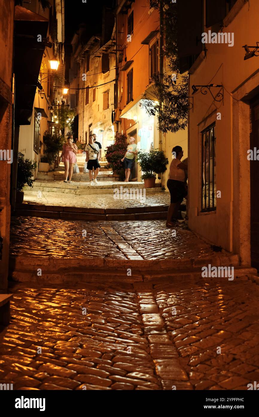 Altstadt schmaler Gasse in Rovinj, Istrien am Abend. Die Leute schlendern entlang alter Steinhäuser. Straßenlaternen reflektieren die gepflasterten Stufen Stockfoto