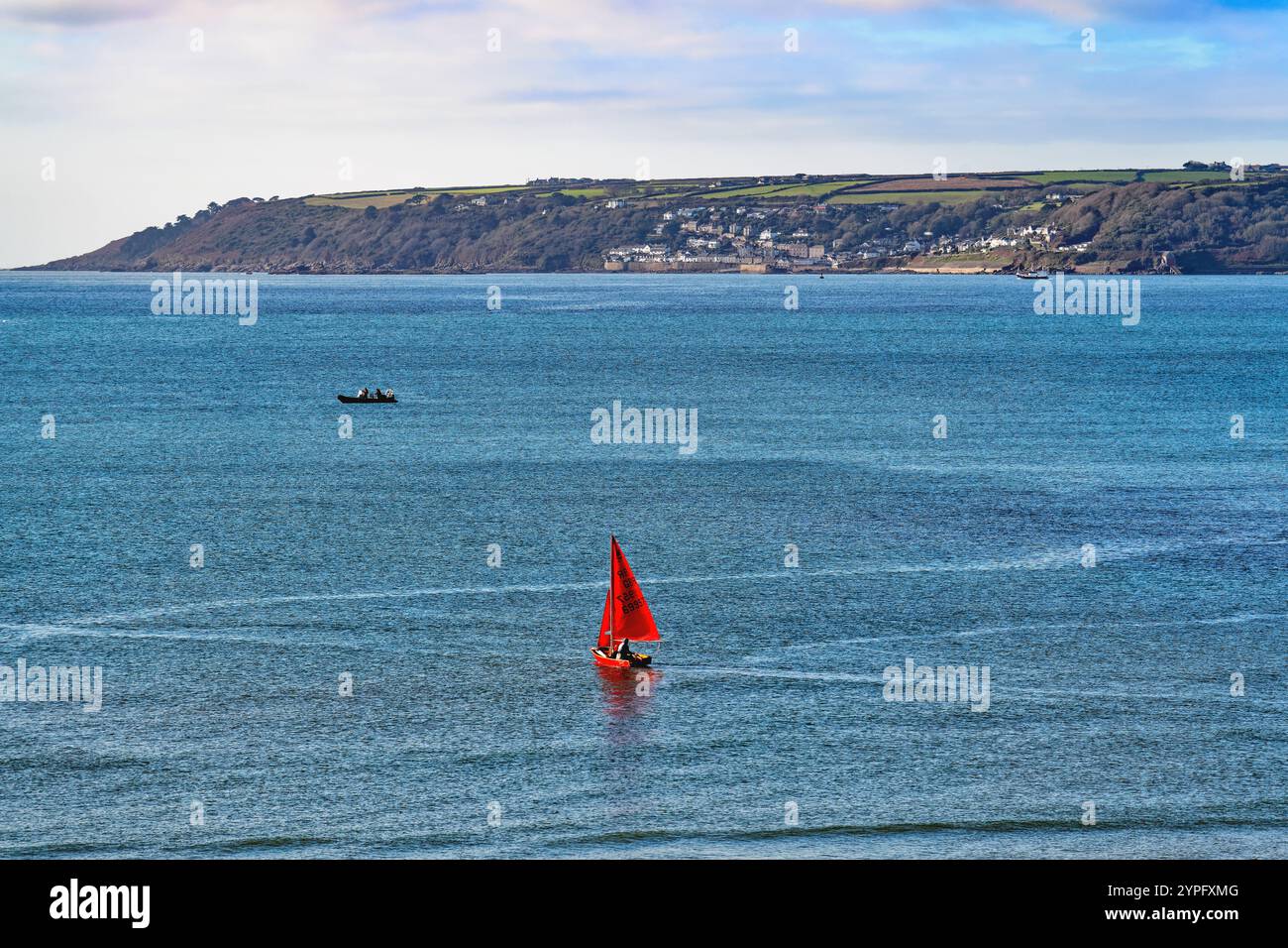 Ein kleiner Segelschmuck mit roten Segeln, der an einem sonnigen Tag auf der Mounts Bay vor dem blauen Meer segelt Penzance Cornwall England UK Stockfoto