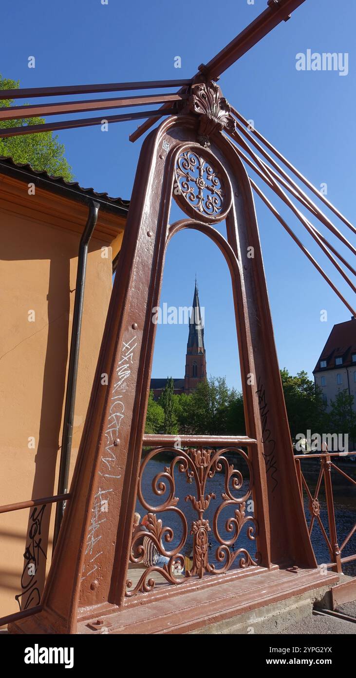 Uppsala, Schweden, 18. Juni 2024. Der Glockenturm ist durch das Metallscharnier einer Brücke über den Kanal zu sehen. Stockfoto