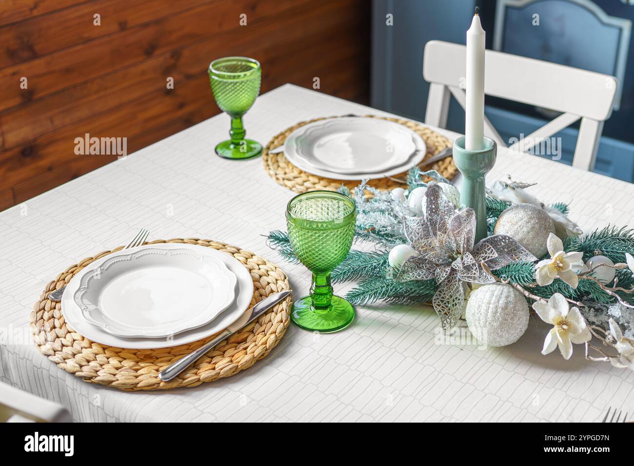 Ein wunderschön gestalteter Weihnachtstisch verfügt über grüne Glasbecher, stilvolle Teller und ein festliches Herzstück. Der gemütliche Essbereich ist dekoriert Stockfoto