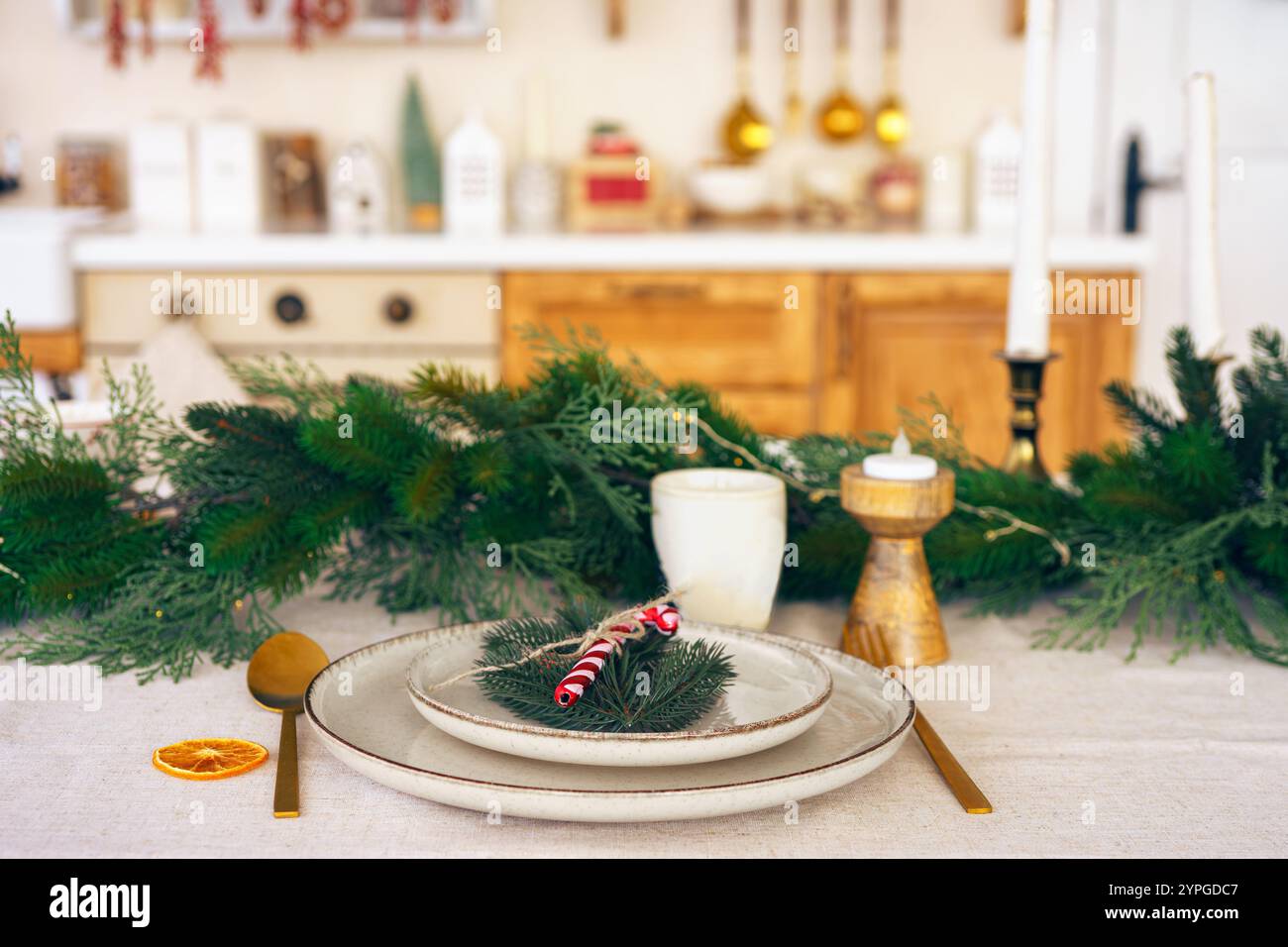 Elegante Weihnachtsfeiertagstisch mit Grün und schlichtem Dekor auf gemütlichem Küchenhintergrund. Schön angelegter Urlaubstisch mit Tellern, ca. Stockfoto