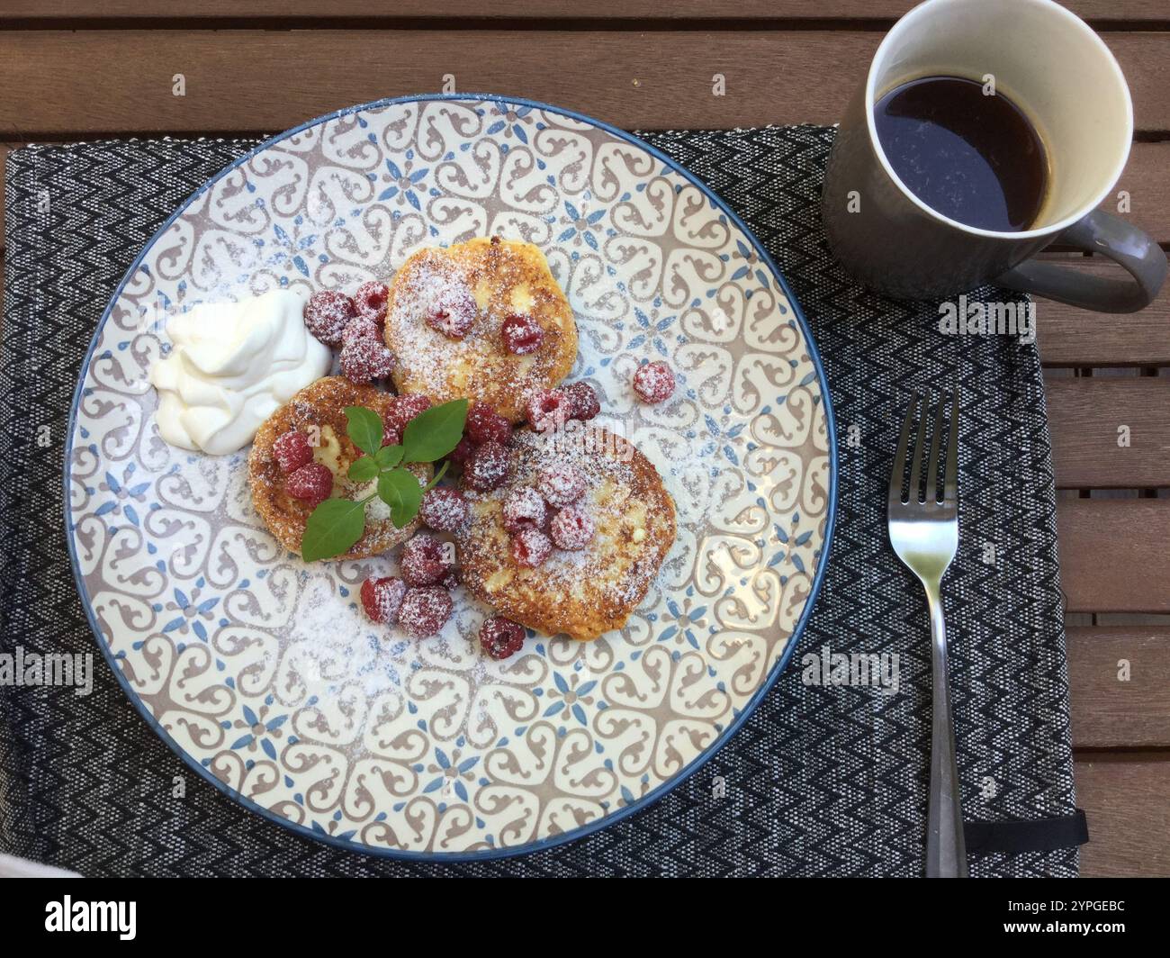 Ein herrliches Frühstücksrestaurant mit süßen Pfannkuchen mit Puderzucker und frischen Beeren, begleitet von einer Tasse Kaffee. Das Essen wird serviert Stockfoto