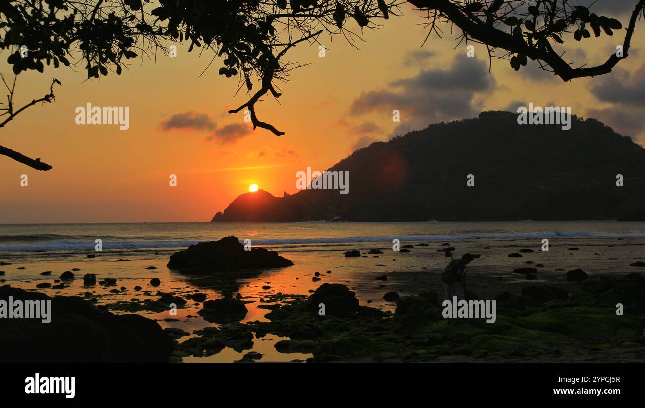 Sonnenuntergang an einem ruhigen Strand mit dunklen und körnigen Schatten auf den Felsen. Stockfoto