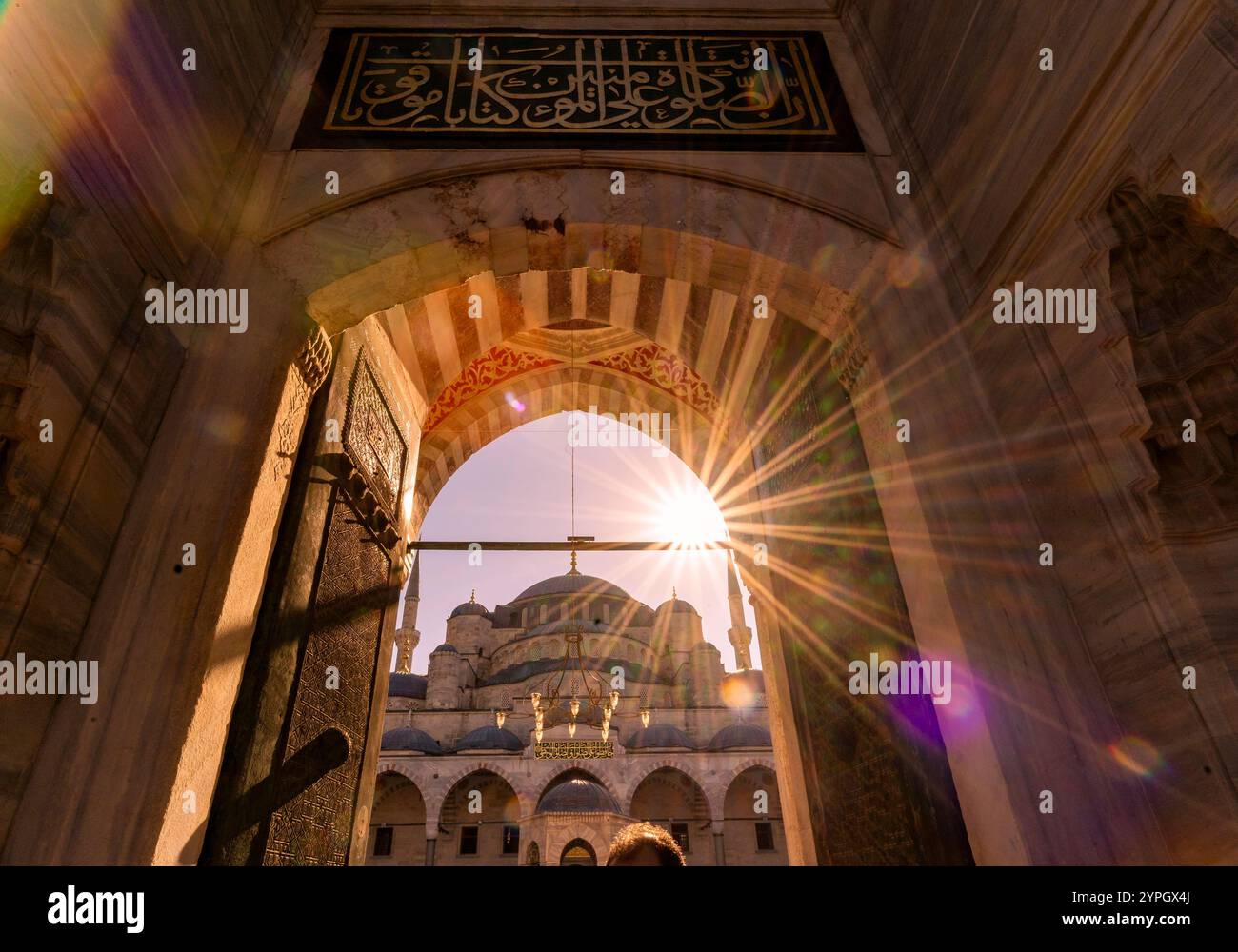 Istanbul, TR - 23. Okt. 2024 Sonnenaufgang in der Blauen Moschee umrahmt seine majestätischen Kuppeln und Bögen durch eine kunstvolle Eingangstür mit goldenen Sonnenstrahlen Stockfoto