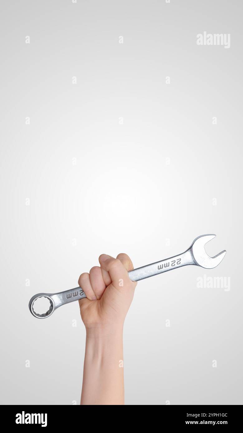 Mit der Hand einen Schraubenschlüssel hoch vor grauem Hintergrund halten, vertikale Komposition mit freiem Platz für Werbetexte, ideal für Werkzeug-Branding oder Indexierung Stockfoto
