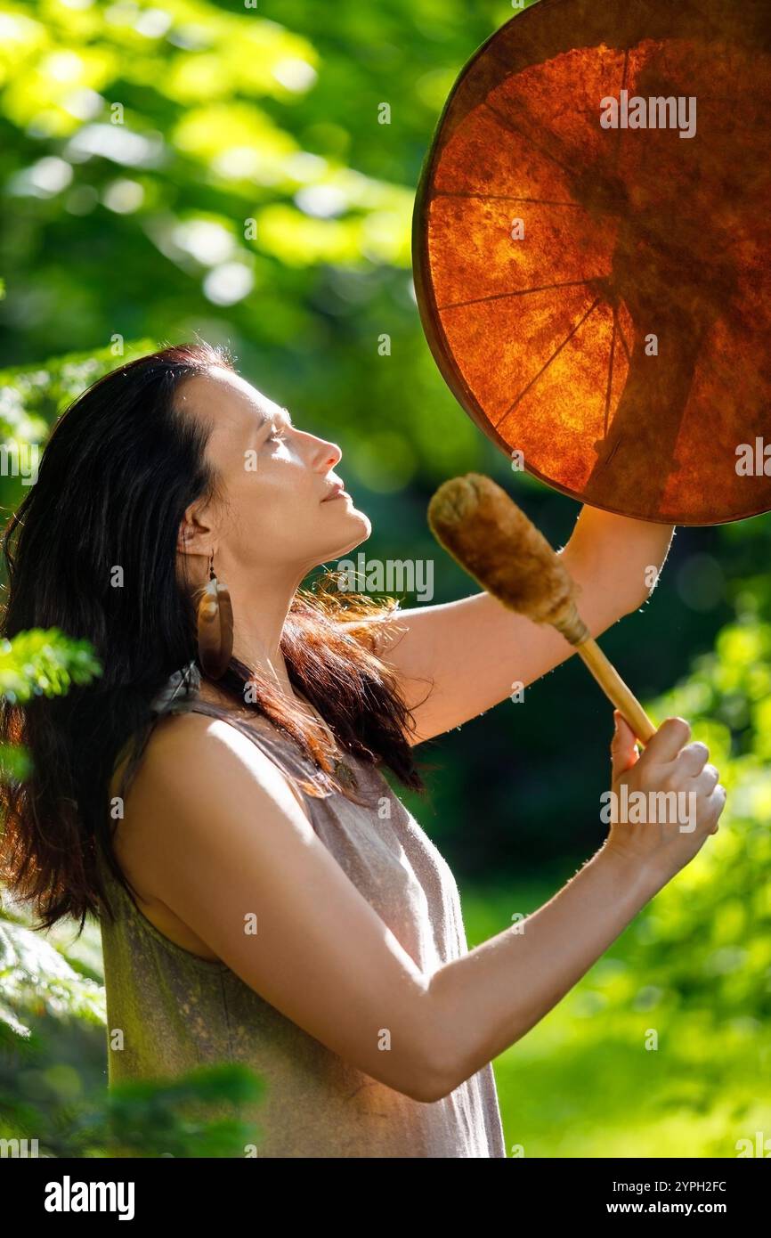 Weibliche Schamanin, die ein authentisches Ritual macht, bei Sonnenuntergang im Wald Geister mit Tambourin zu beschwören Stockfoto