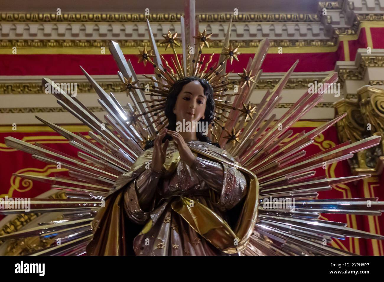 Cospicua, Malta - 28. November 2024. Atemberaubende religiöse Statue mit strahlendem Metallic Starburst Design in lebendiger Umgebung Stockfoto