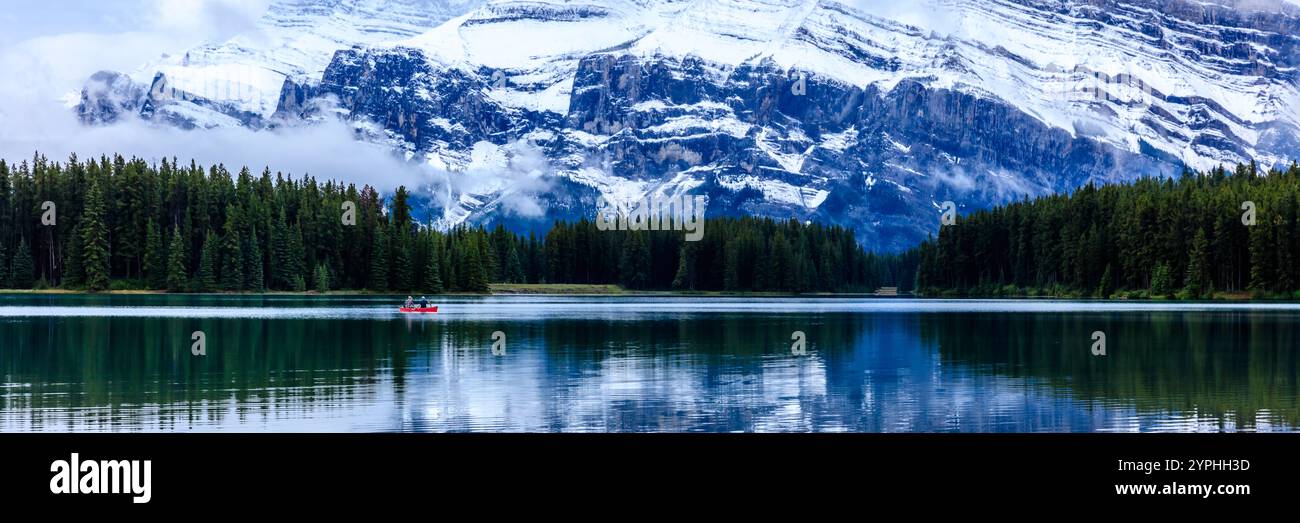 Ein Mann in einem roten Kanu paddelt auf einem See vor einem Berg. Die Szene ist friedlich und ruhig, der Mann genießt die Schönheit der Natur Stockfoto