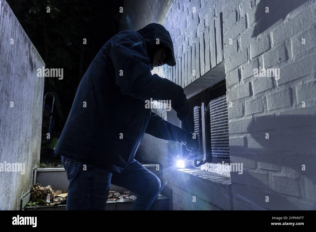 Symbolisches Bild eines Hauseinbruchs: Der Täter nähert sich einem Haus von der Gartenseite und versucht, ein Kellerfenster aufzubrechen, um in die Halle zu gelangen Stockfoto