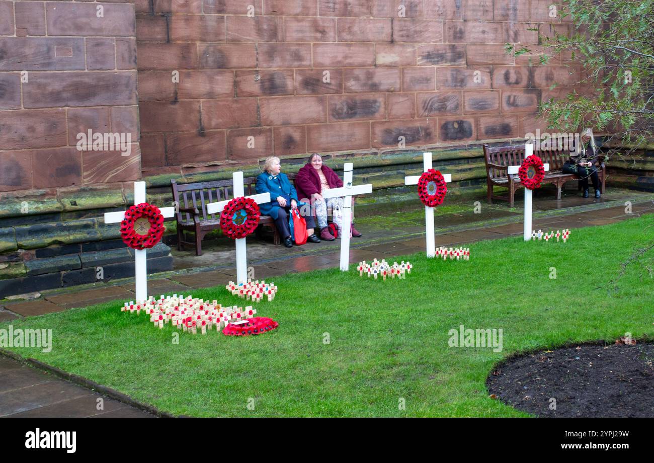 Die Menschen sitzen nach dem Gedenktag im Garten der Chester Cathedral Cheshire zwischen Mohnkreuzen. Stockfoto