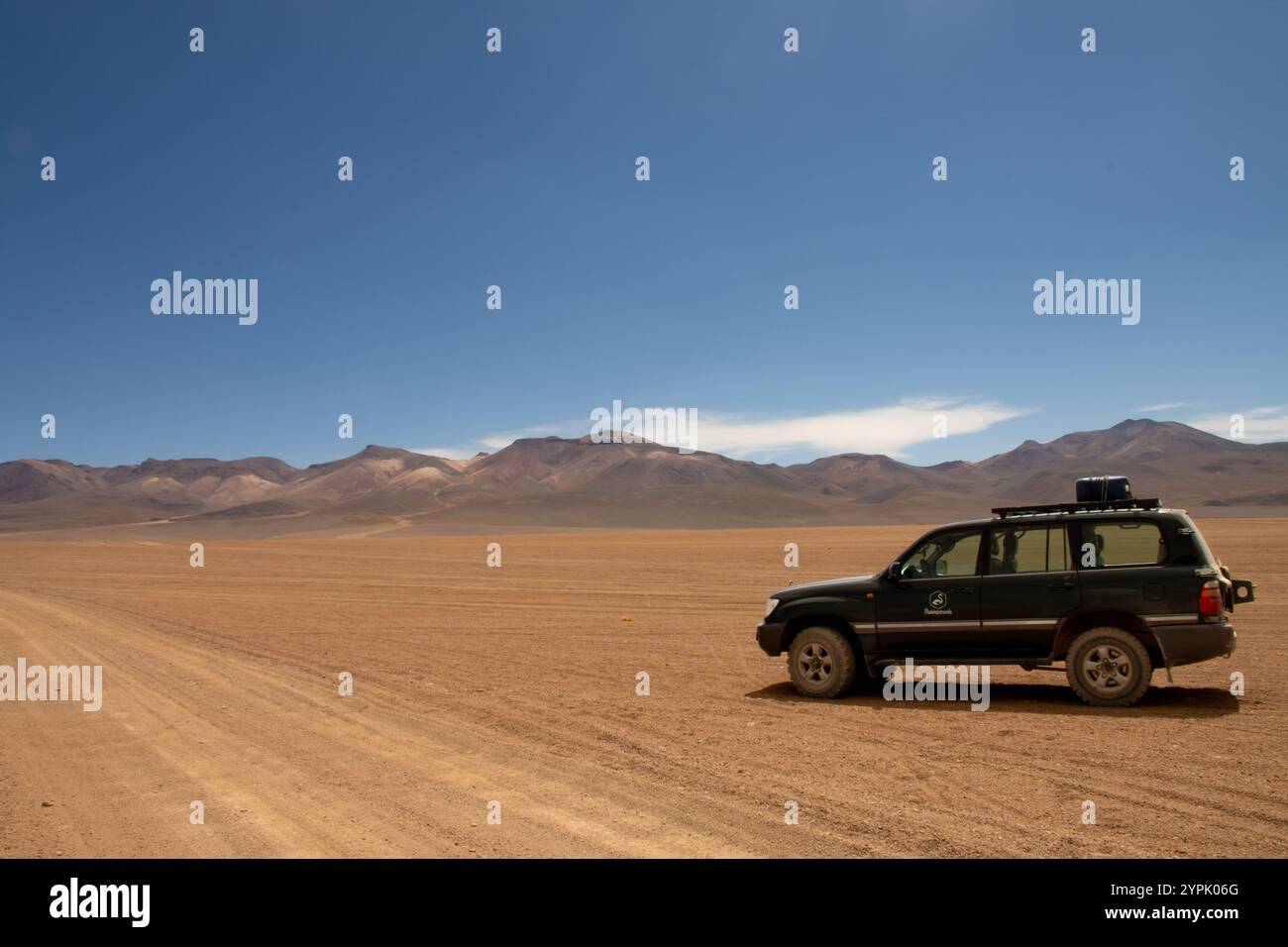Geländewagen in der weiten Wüstenlandschaft des bolivianischen Altiplano, umgeben von trockenen Ebenen und majestätischen Bergketten unter klarem blauem Himmel Stockfoto