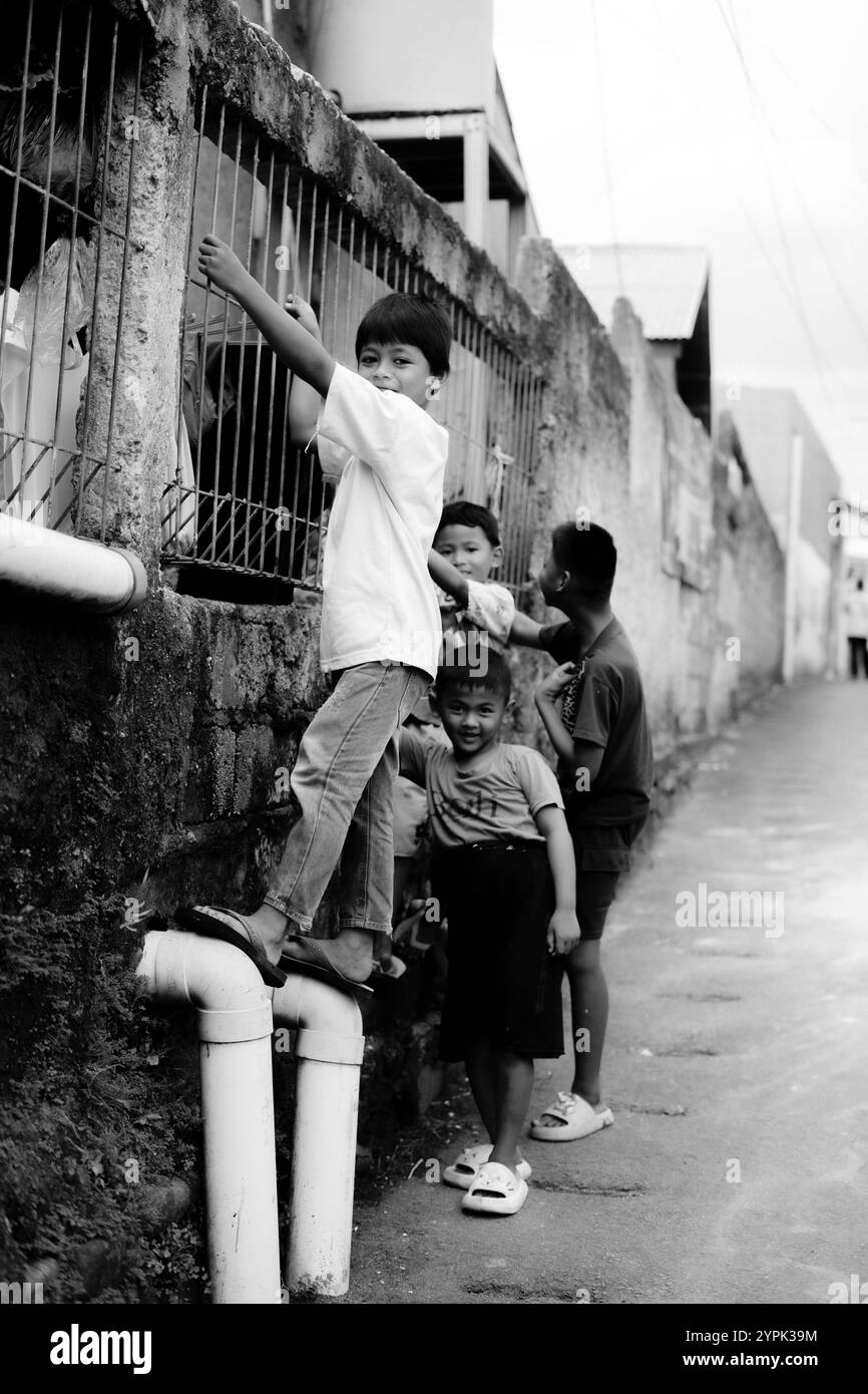 Bogor, 24. November 2024. Vier kleine Kinder stehen zusammen in einer engen Gasse, lächeln und schauen sich in einer lebhaften Umgebung um Stockfoto