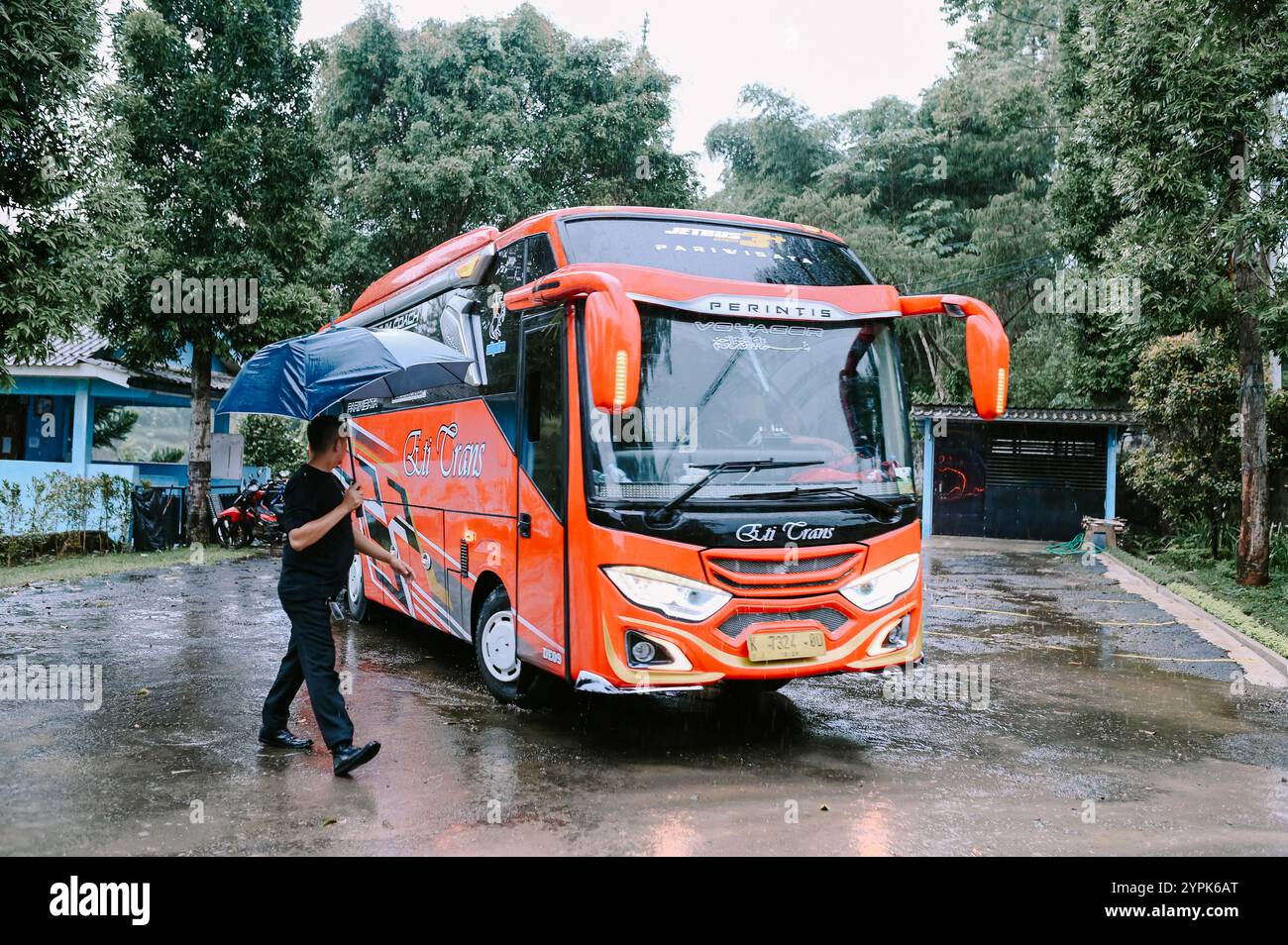 Bogor, 18. November 2024. Ein roter Bus fährt in den Parkplatz einer Villa, umgeben von üppigem Grün und landschaftlich reizvoller Umgebung Stockfoto