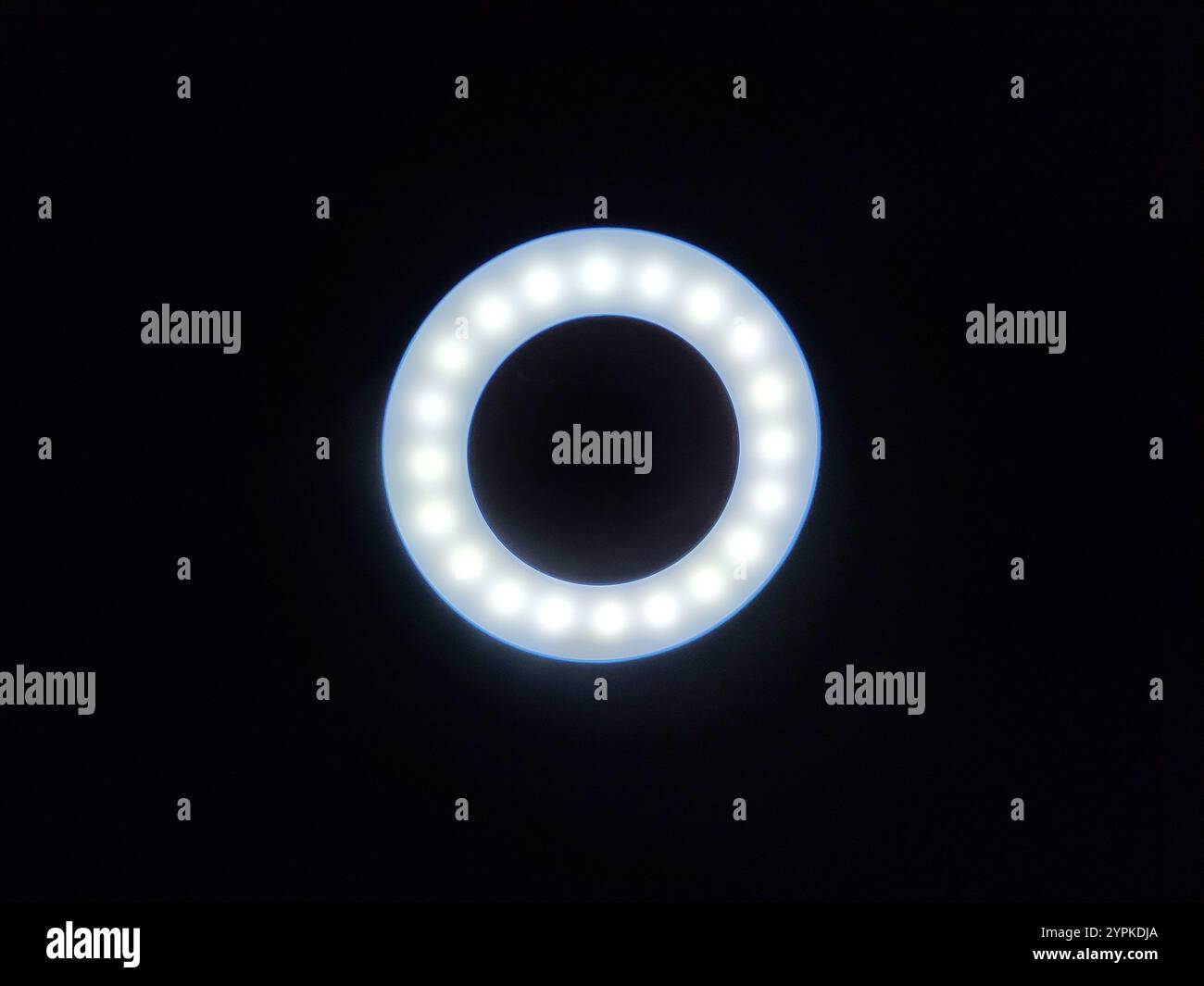 Ein kreisförmiges LED-Ringlicht leuchtet sanft vor dunklem Hintergrund, mit gleichmäßig angeordneten Lampen, die ideal für Fotografie, Videoaufnahmen oder die Erstellung von Inhalten sind. Stockfoto