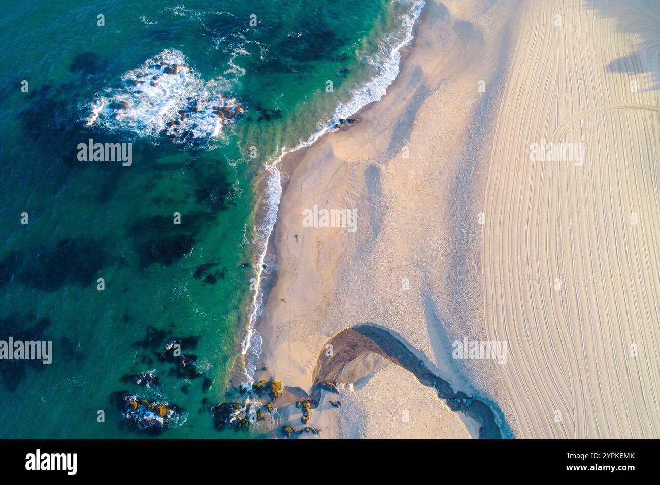 Von oben auf einen Strand mit einem kleinen Bach, der ins Meer fließt, Drohnenfotografie Stockfoto