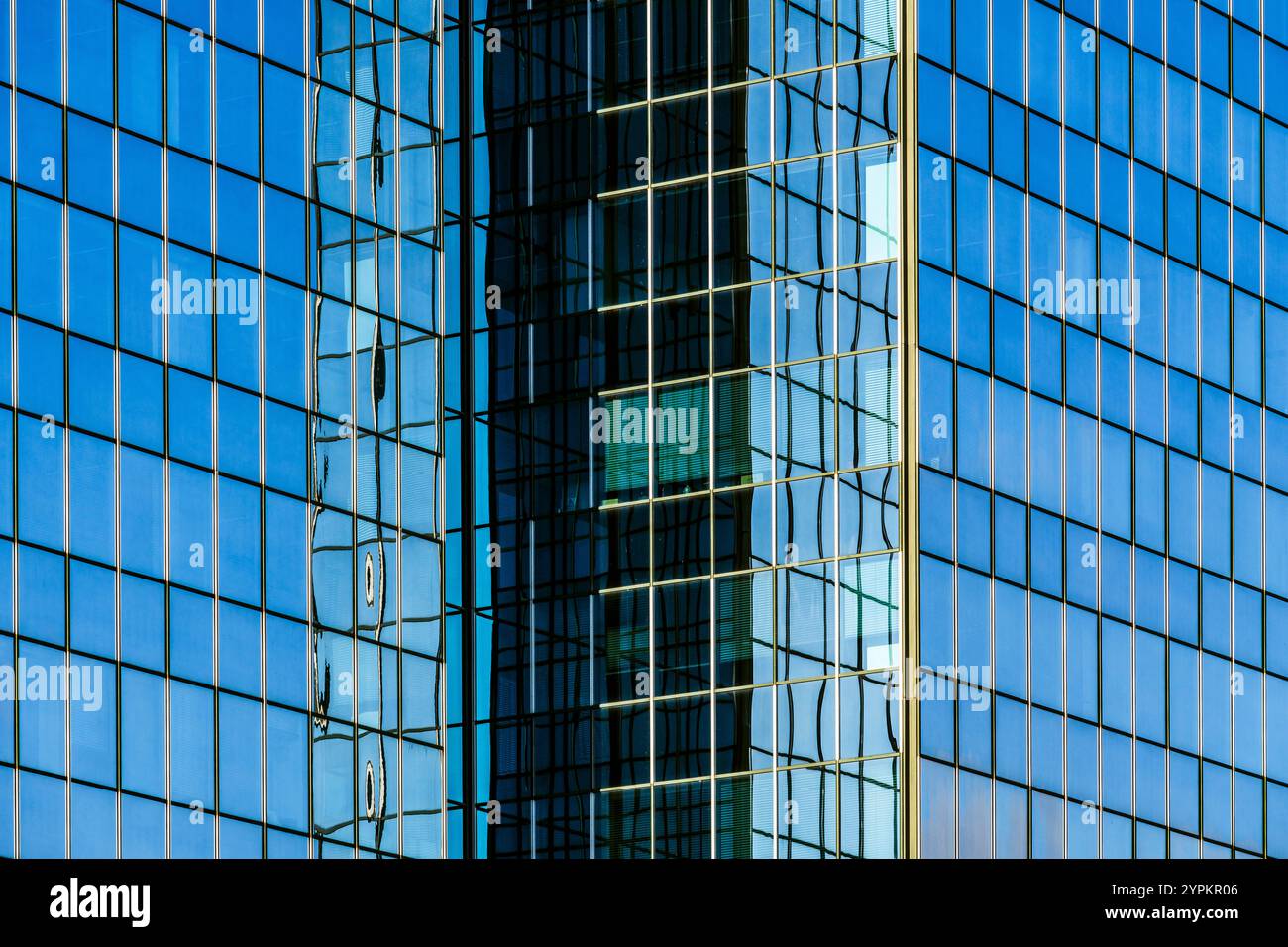 Moderne Glasfassade mit symmetrischen Mustern und Reflexen unter dem blauen Himmel Stockfoto