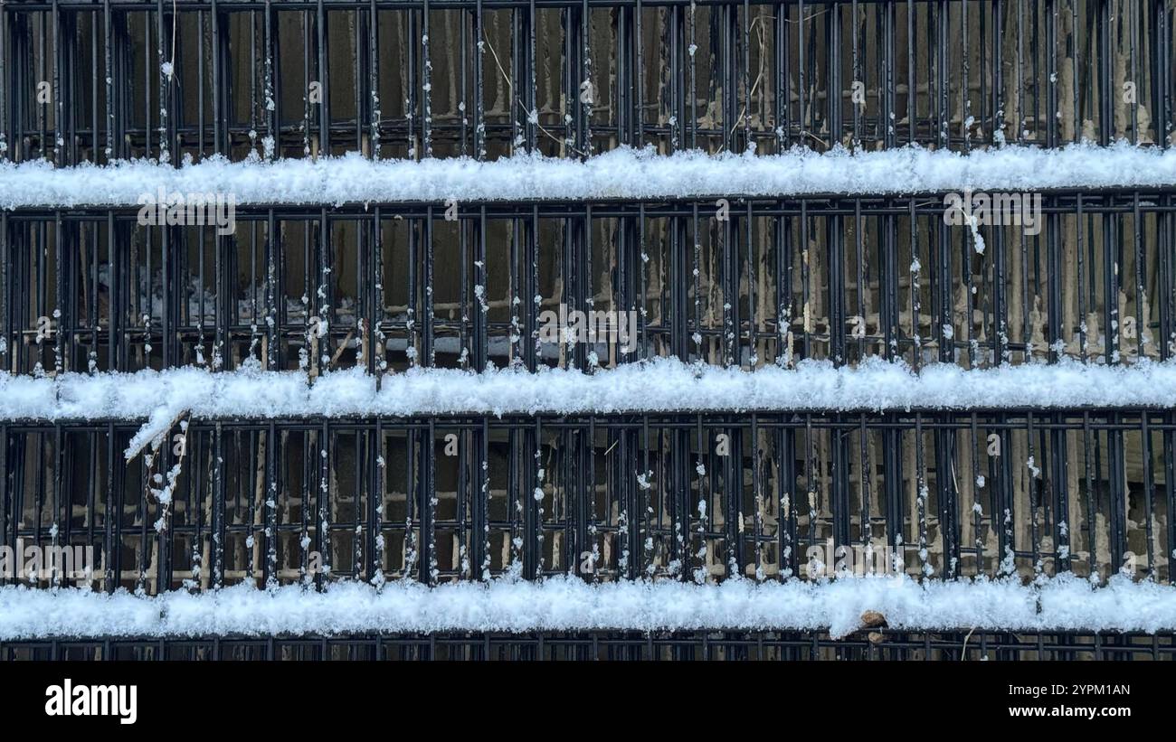 Eine Nahaufnahme zeigt einen Bereich aus schwarzem Metallgitter, in dem sich Schnee auf den horizontalen Balken ansammelt. Der Hintergrund ist teilweise durch die sichtbar Stockfoto