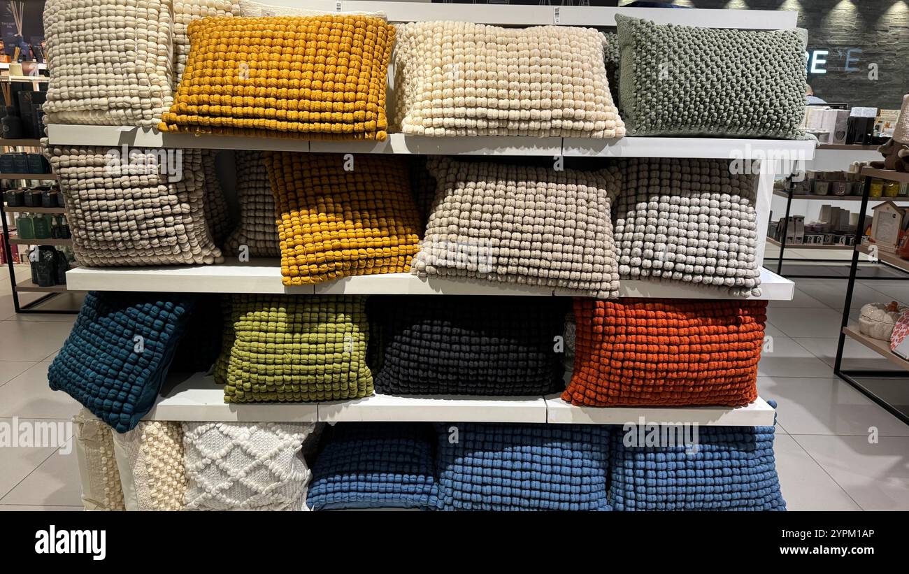 Eine Einzelhandelsausstellung mit zahlreichen strukturierten Kissen in verschiedenen Farben und Größen, die ordentlich auf weißen Regalen angeordnet sind. Die Kissen sind hauptsächlich n Stockfoto