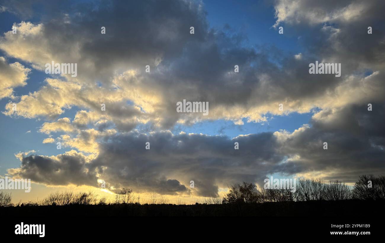Eine weite Aufnahme zeigt einen meist bewölkten Himmel bei Sonnenuntergang. Graue und dunkle Wolken dominieren, hellere, gelbliche Wolken am Horizont sichtbar. Silhouette Stockfoto
