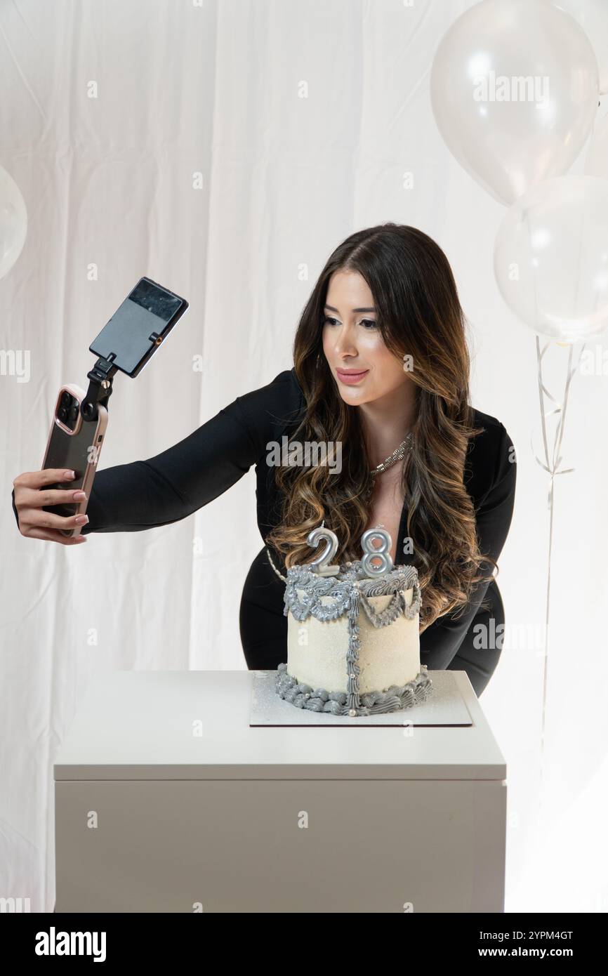 Eine Frau macht ein Foto von einem Kuchen mit Silber-weiß-Zuckerguss. Auf dem Kuchen ist ein silberfarbenes und weißes Design Stockfoto