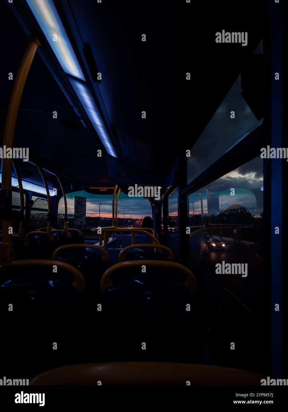 Moody Interior of an Leere Bus at Twilight, der entfernte Straßenlaternen und urbane Skyline-Reflektionen einfängt Stockfoto