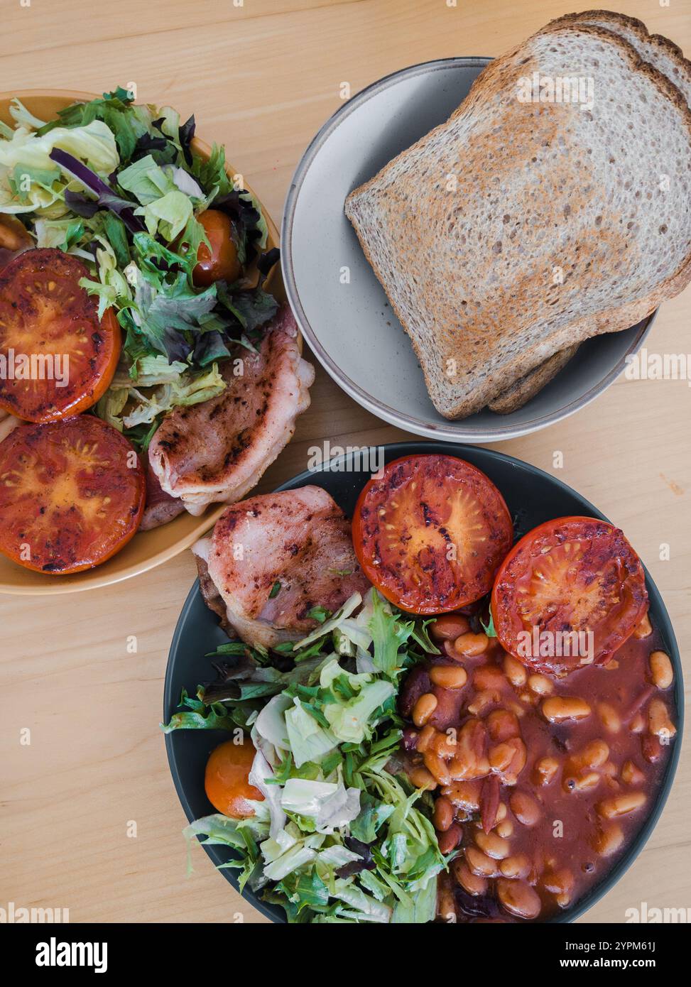 Traditionelles englisches Frühstück mit gegrillten Tomaten, Bohnen, Salat und Toast auf einem Holztisch Stockfoto