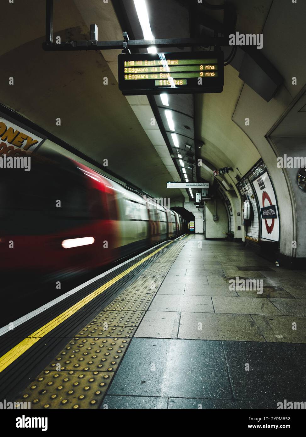 Verschwommene Londoner U-Bahn-Linie, die von einem schwach beleuchteten Bahnsteig von Kennington Station abfährt Stockfoto