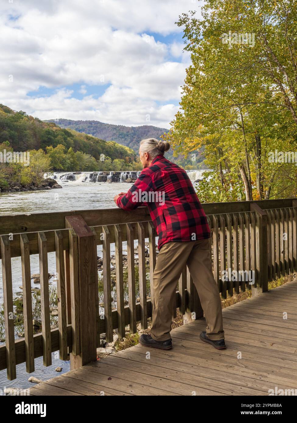 Ein Mann in roter Holzfällerjacke und Haarbrötchen bewundert die Sandstone Falls, umgeben von den lebhaften Herbstfarben des New River Gorge National Pa Stockfoto