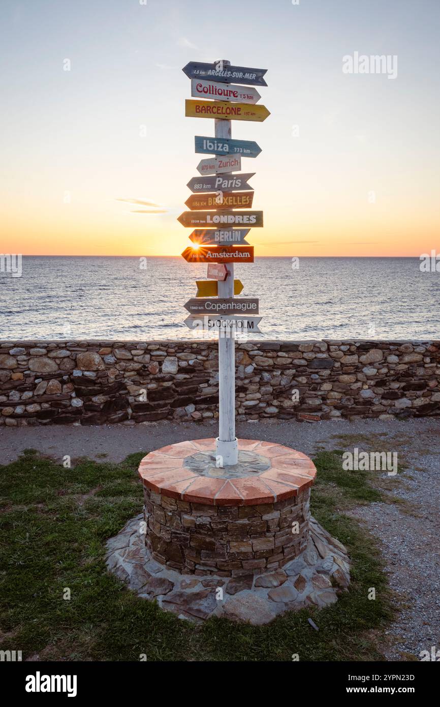 Sonnenaufgang hinter einem Wegweiser mit europaweiten Entfernungsschildern in der Nähe von Collioure, Cote Vermeille, Okzitania, Languedoc-Roussillion, Frankreich Stockfoto