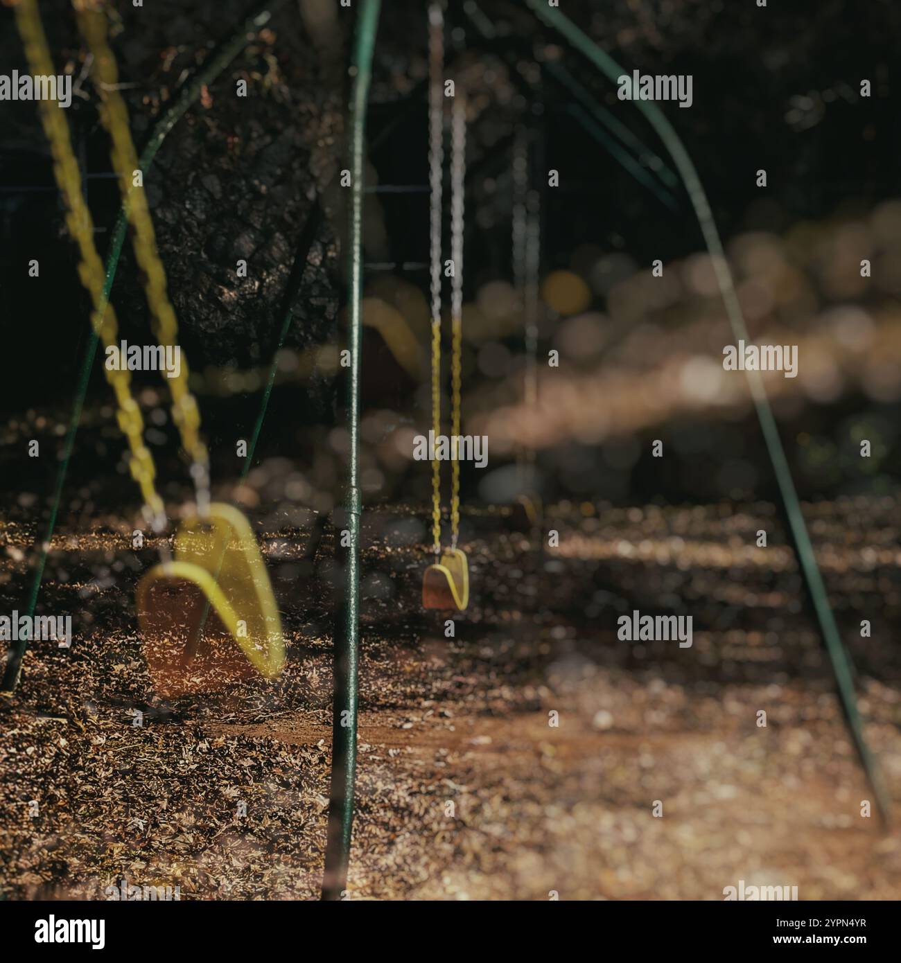 Herbstlaub bedecken den Boden unter einem leeren Schaukel auf dem Spielplatz und schaffen eine ruhige und leicht nostalgische Atmosphäre. Weiche Sonnenlichtfilter. Stockfoto