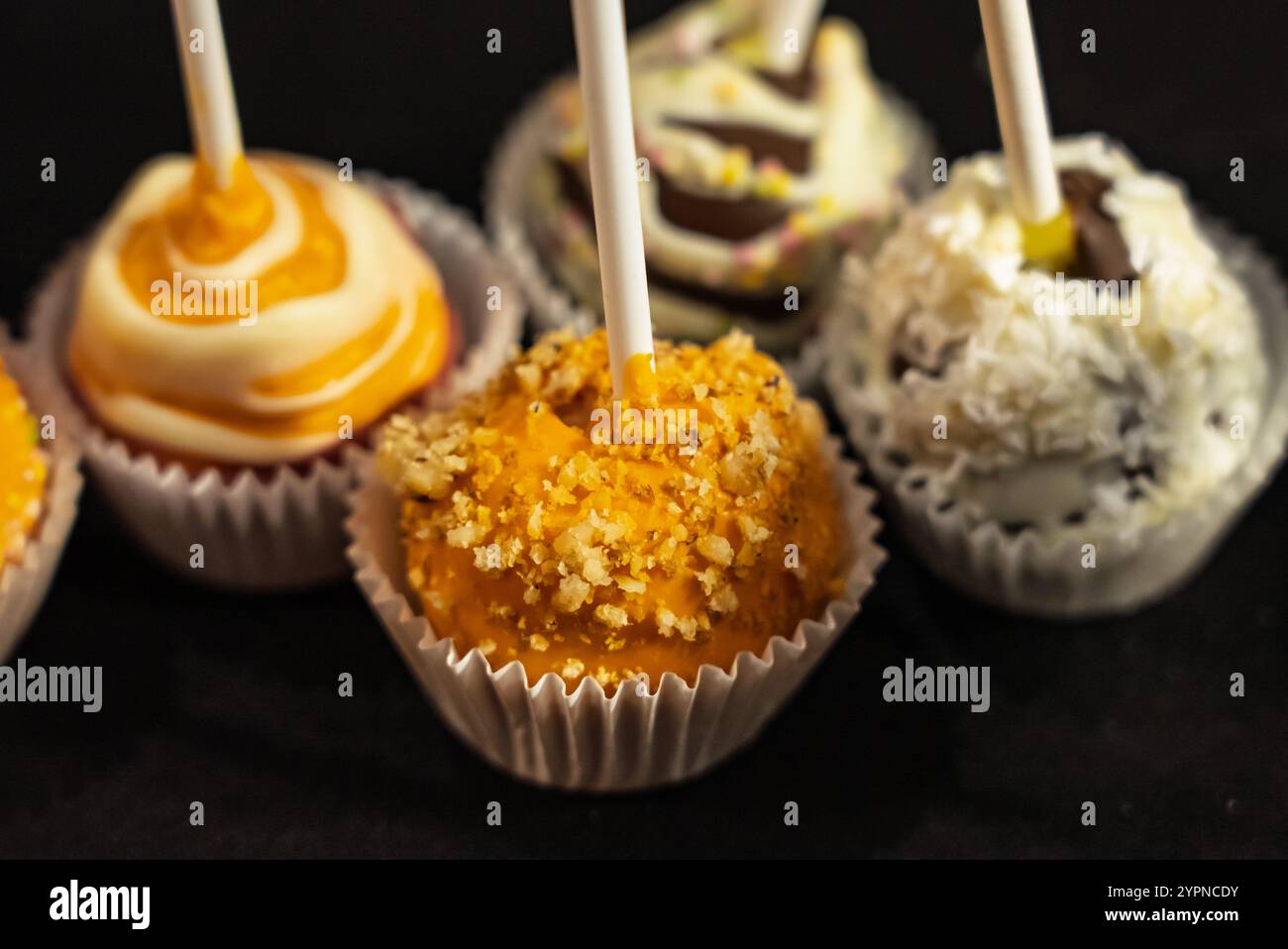 Dekorative Schokoladen auf Sticks mit leuchtenden Farben und Belägen, die auf einem übersichtlichen Ausstellungsstand angeordnet sind. Bunte Schokoladenlutscher mit Schokoladenspäne Stockfoto