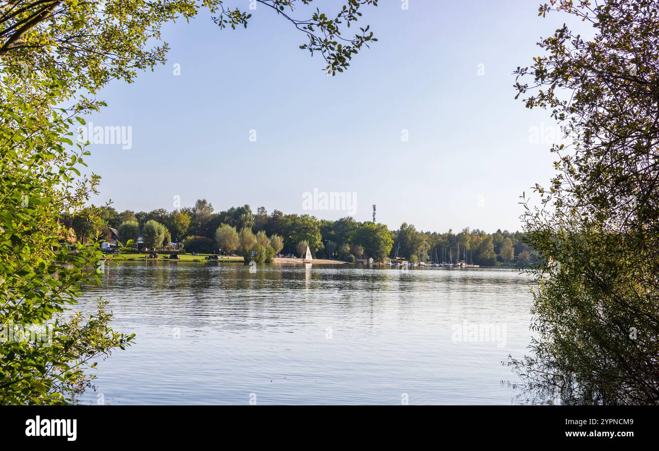 Ein ruhiger Blick auf den See mit einem Sandstrand, Segelbooten und üppigen grünen Bäumen unter dem Himmel, die eine Outdoor-Szene zeigen. Gronau, Deutschland, 2024 Stockfoto