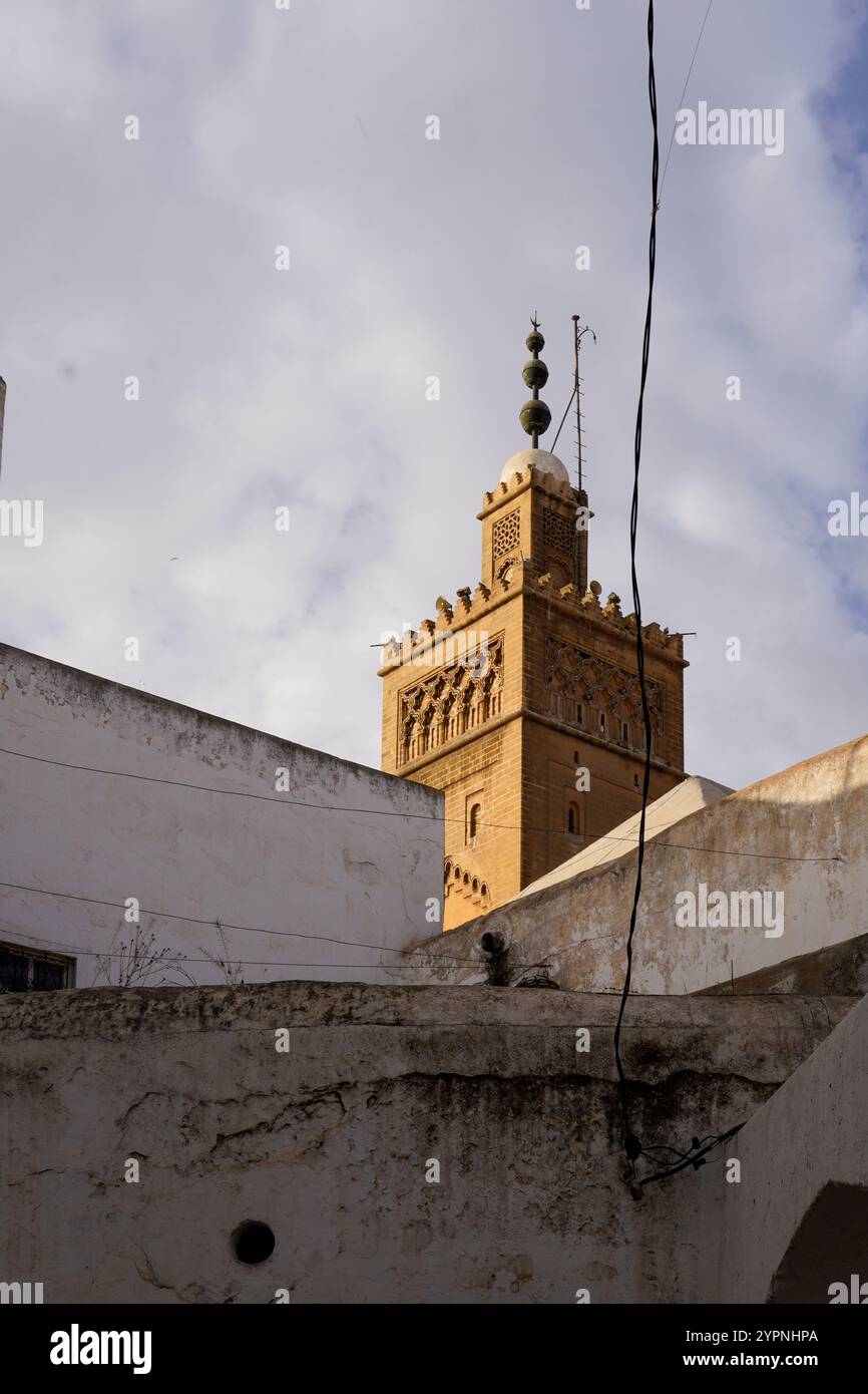 Traditionelles Minarett der Moschee vor einem teilweise bewölkten Himmel, das seine komplexen architektonischen Details und dekorativen Elemente hervorhebt. Stockfoto