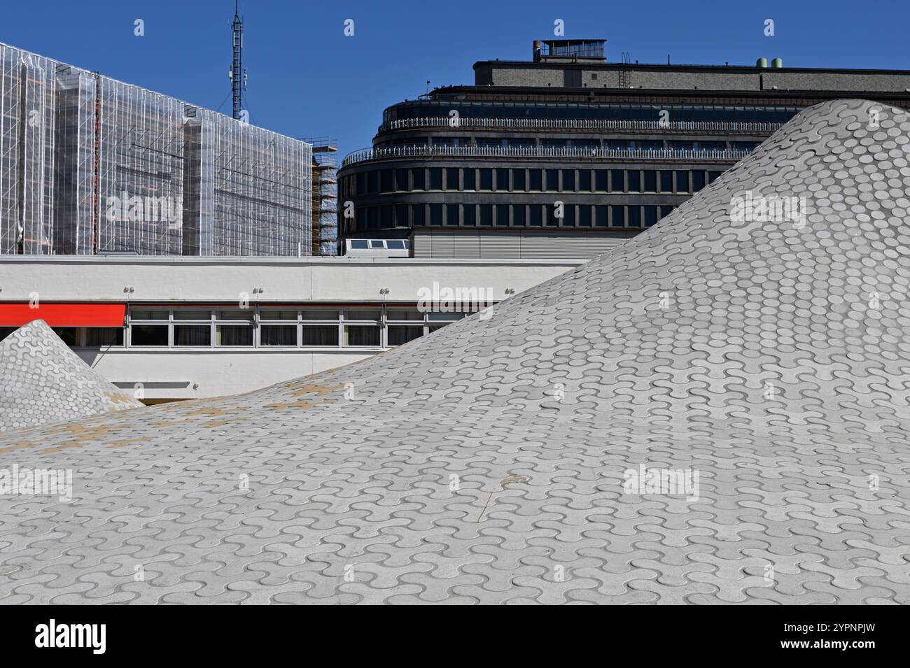 Eine moderne Architekturszene, die ein einzigartiges, hügeliges Dachdesign aus ineinander greifenden Fliesen betont. Die wellige Oberfläche erzeugt einen visuellen Streifen Stockfoto