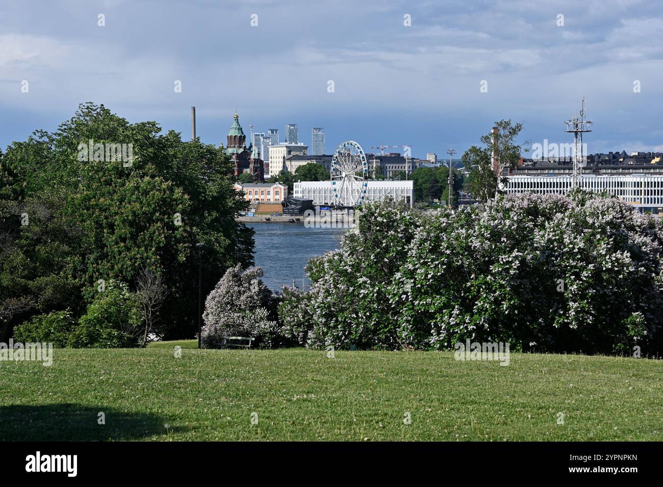 Ein malerischer Blick auf Helsinki, Finnland, mit üppigen grünen Parks im Vordergrund, lebendigen blühenden Büschen und der Uferpromenade mit berühmten Landma Stockfoto