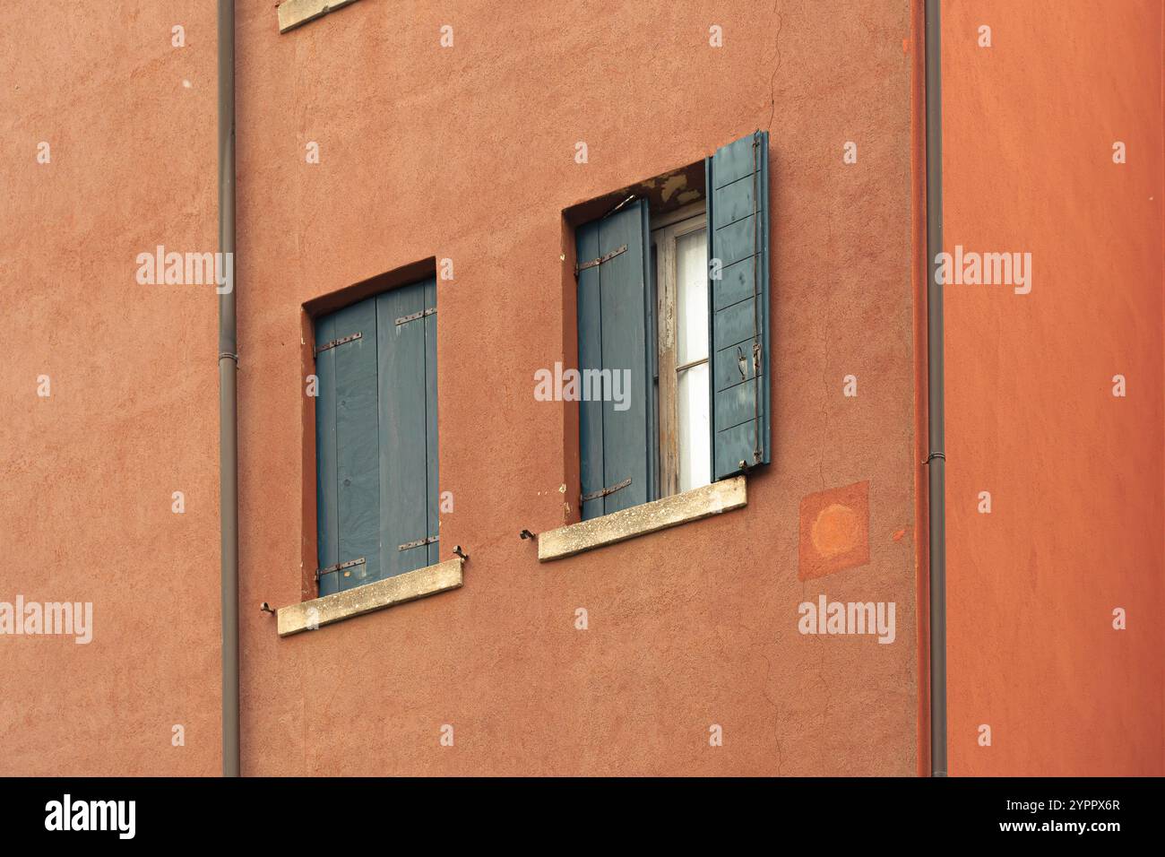 Verwitterte orangefarbene Wand mit blauen Fensterläden Stockfoto