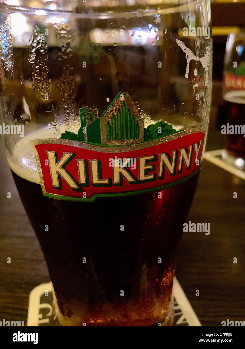 Ein halb leeres Glas Kilkenny Bier auf dem Tisch eines Pubs Stockfoto