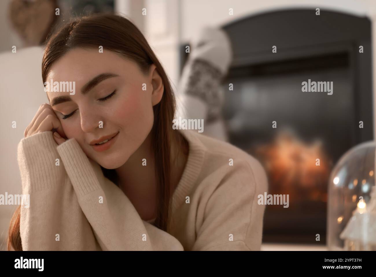 Frau in warmem Pullover, die zu Hause neben dem Kamin ruht Stockfoto