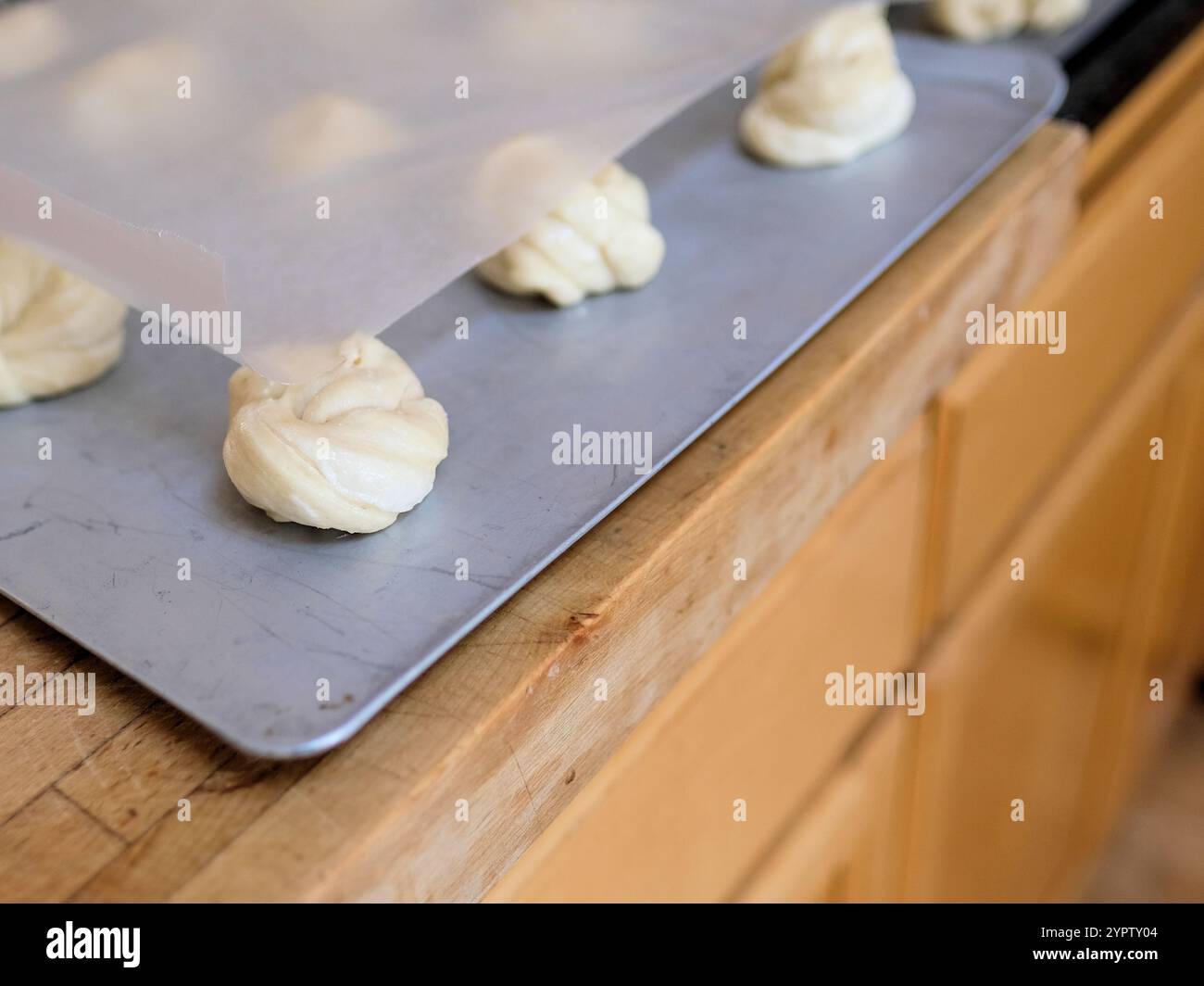 Zum Abendessen gebundene Hefe-Brötchen, die in Knoten auf einer Metallplatte liegen und beweisen, während der Teig vor dem Backen im Ofen aufgeht. Stockfoto