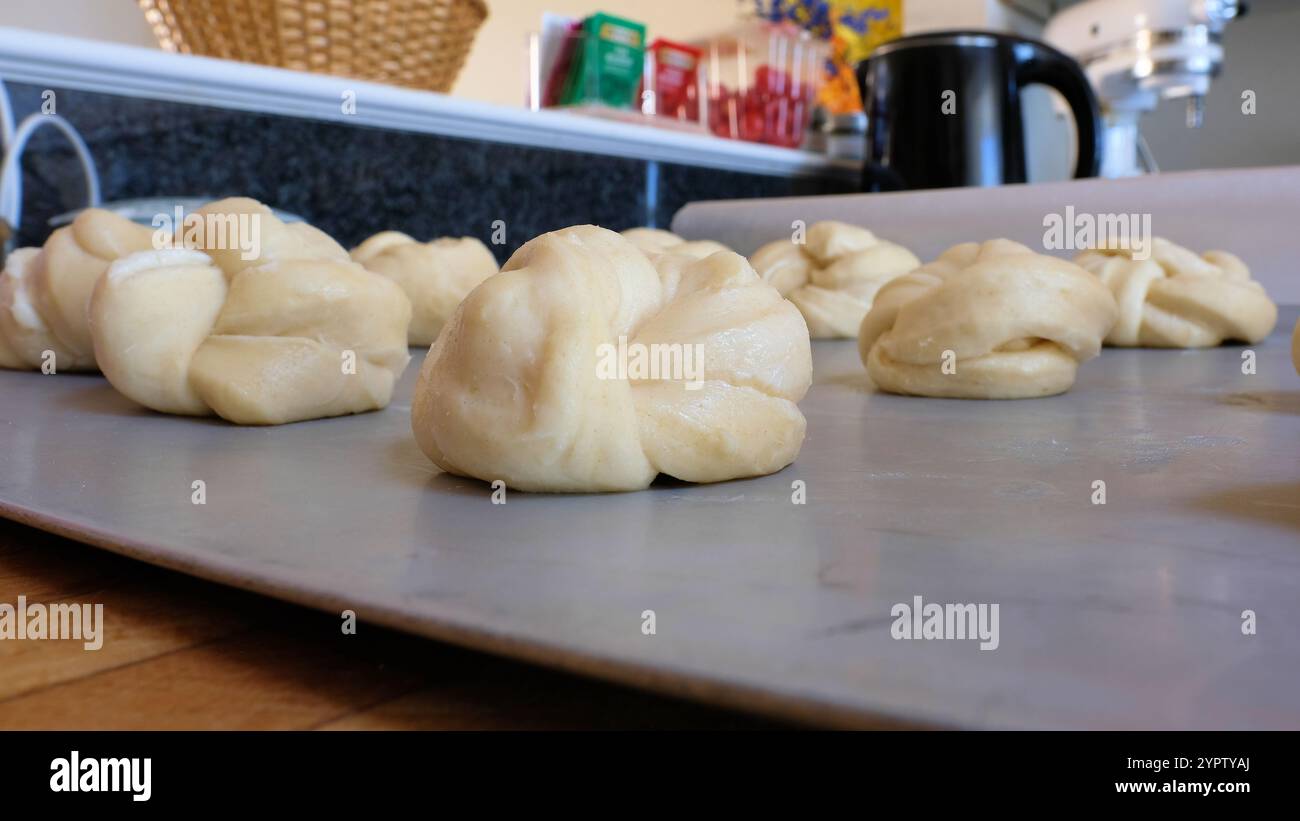 Zum Abendessen gebundene Hefe-Brötchen, die in Knoten auf einer Metallplatte liegen und beweisen, während der Teig vor dem Backen im Ofen aufgeht. Stockfoto