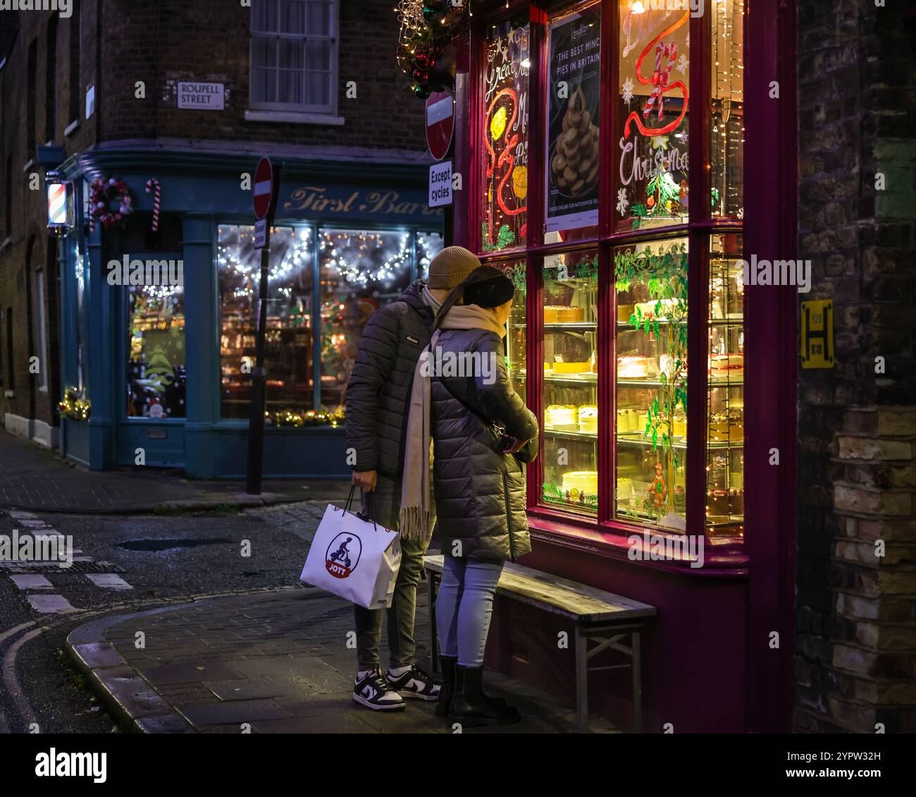 London, Großbritannien. Dezember 2024. Ein paar sehen sich die Kuchen und weihnachtskekse an. Die Konditor Bakery sieht in der historischen Umgebung der ehemaligen georgischen Arbeiterhäuser im Roupell Street Conservation Area in Lambeth festlich aus. Quelle: Imageplotter/Alamy Live News Stockfoto