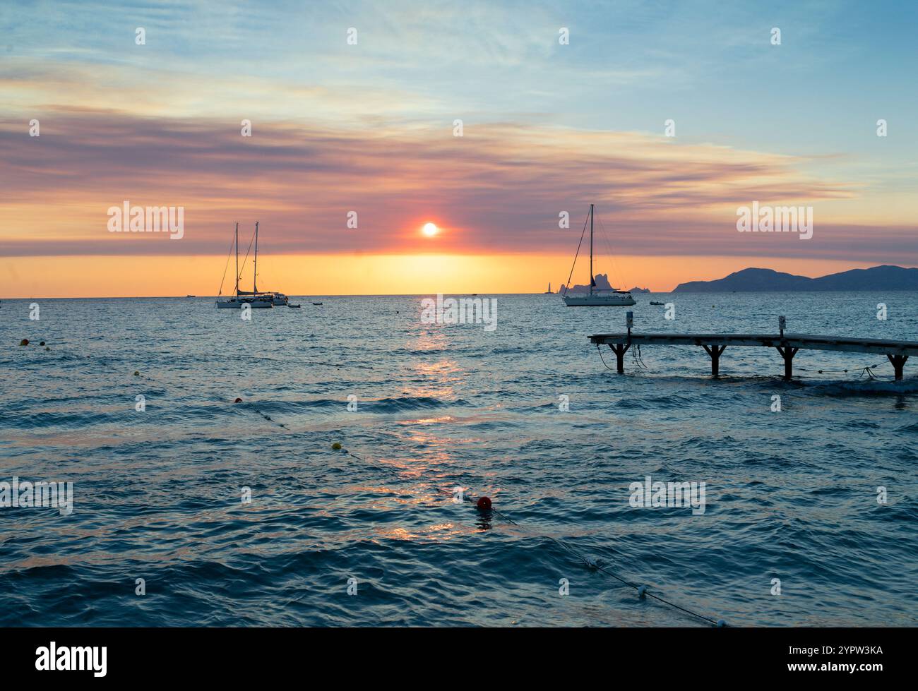 Sonnenuntergang über dem Mittelmeer, warmes Licht auf das Wasser. Zwei Segelboote liegen an der Straße vor einem Strand auf der Insel Formenter an Stockfoto