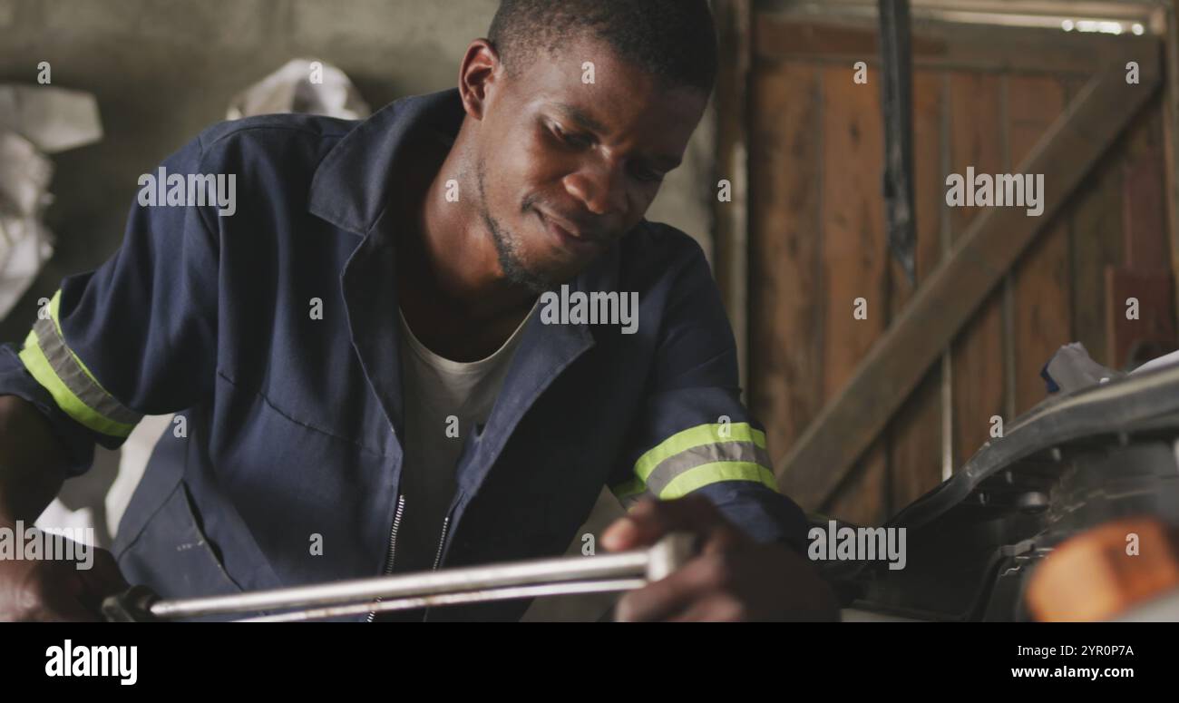 Vorderansicht eines afrikanischen männlichen Automechanikers in einer Werkstätte in der Gemeinde, der ein Auto mit einem Kofferraum repariert Stockfoto