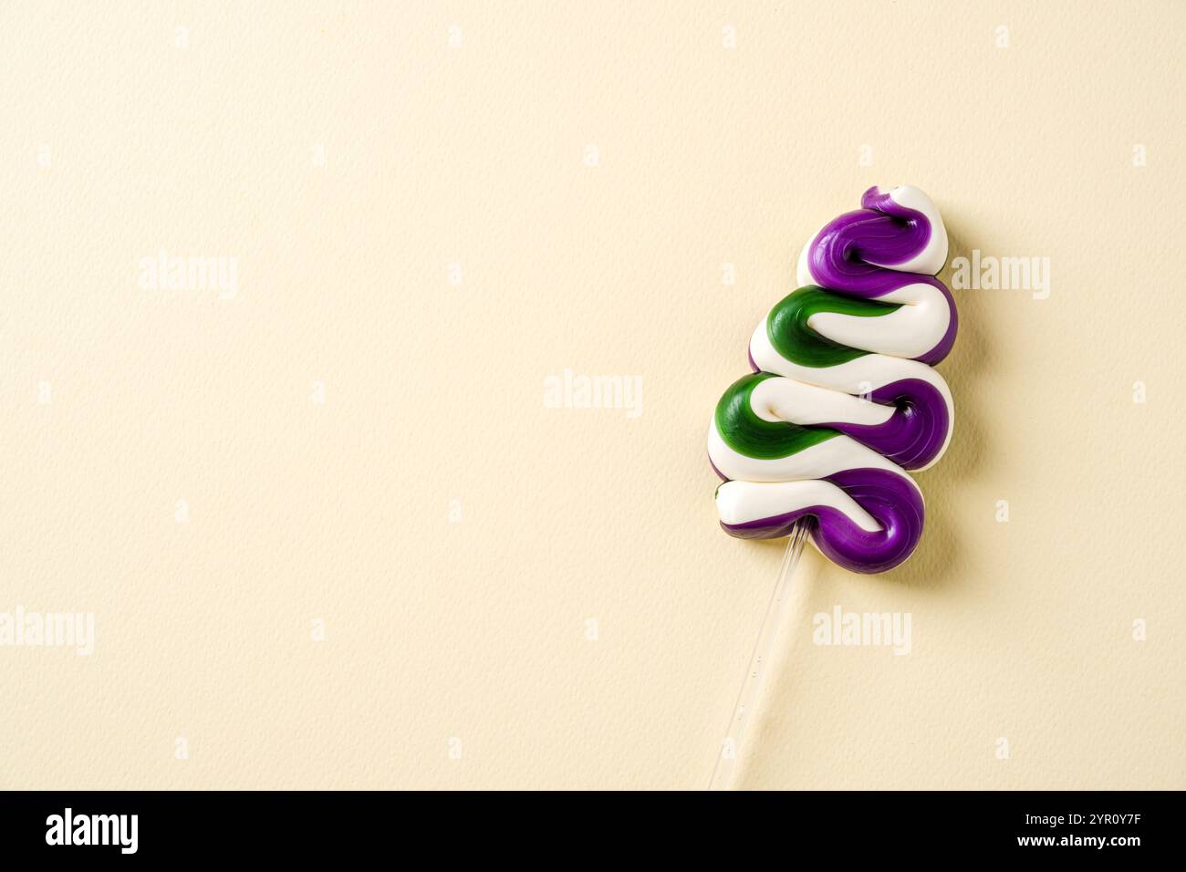 Ein lebendiger, baumförmiger, spiralförmiger Lutscher mit lila, grünen und weißen Farben auf einem minimalistischen Pastellhintergrund Stockfoto