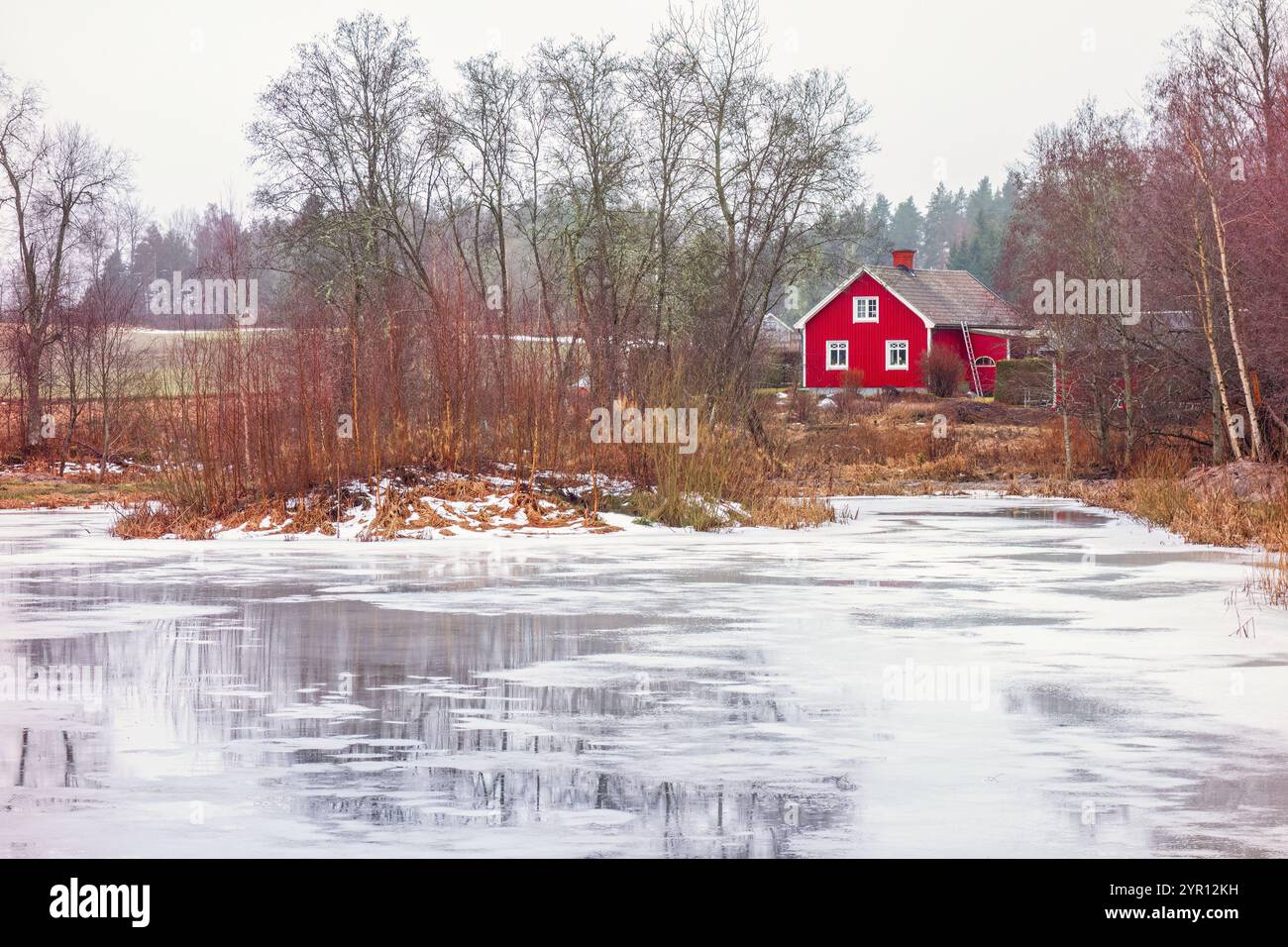 Gefrorener See mit einem roten Haus in der Landschaft Stockfoto