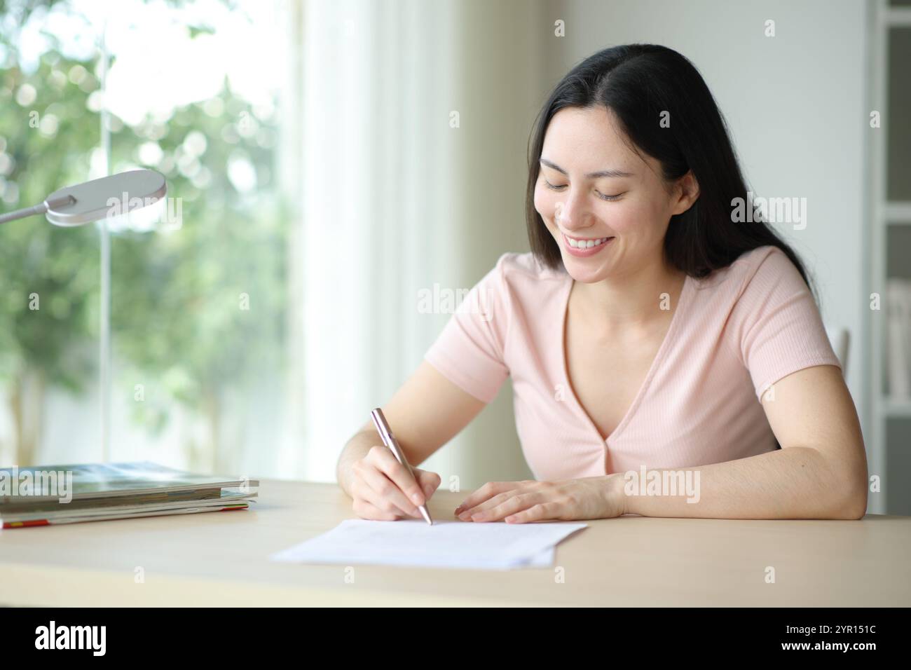 Glückliche asiatische Frau, die in einem Zimmer zu Hause Papier unterschreibt Stockfoto