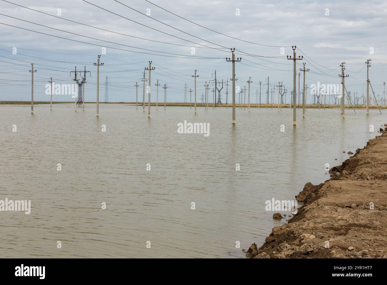 Wasser überschwemmt das Land, während die Strommasten hoch stehen und einen starken Kontrast zum grauen, bewölkten Himmel bilden Stockfoto